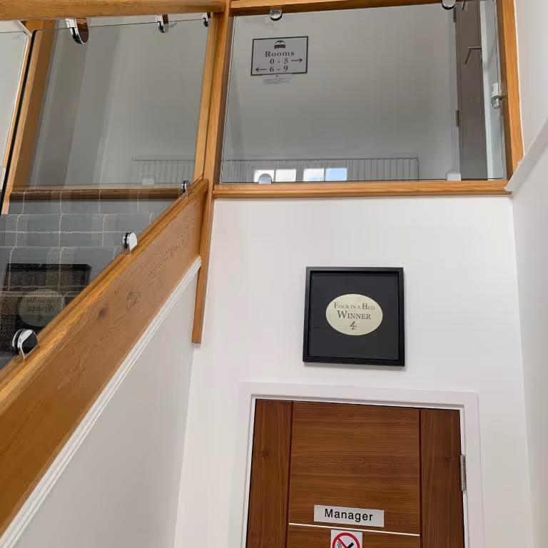 The interior staircase at Rooms At The Inn in Retford, UK. A "Four in a Bed WINNER" award plaque is displayed on the wall next to the Manager's office door.