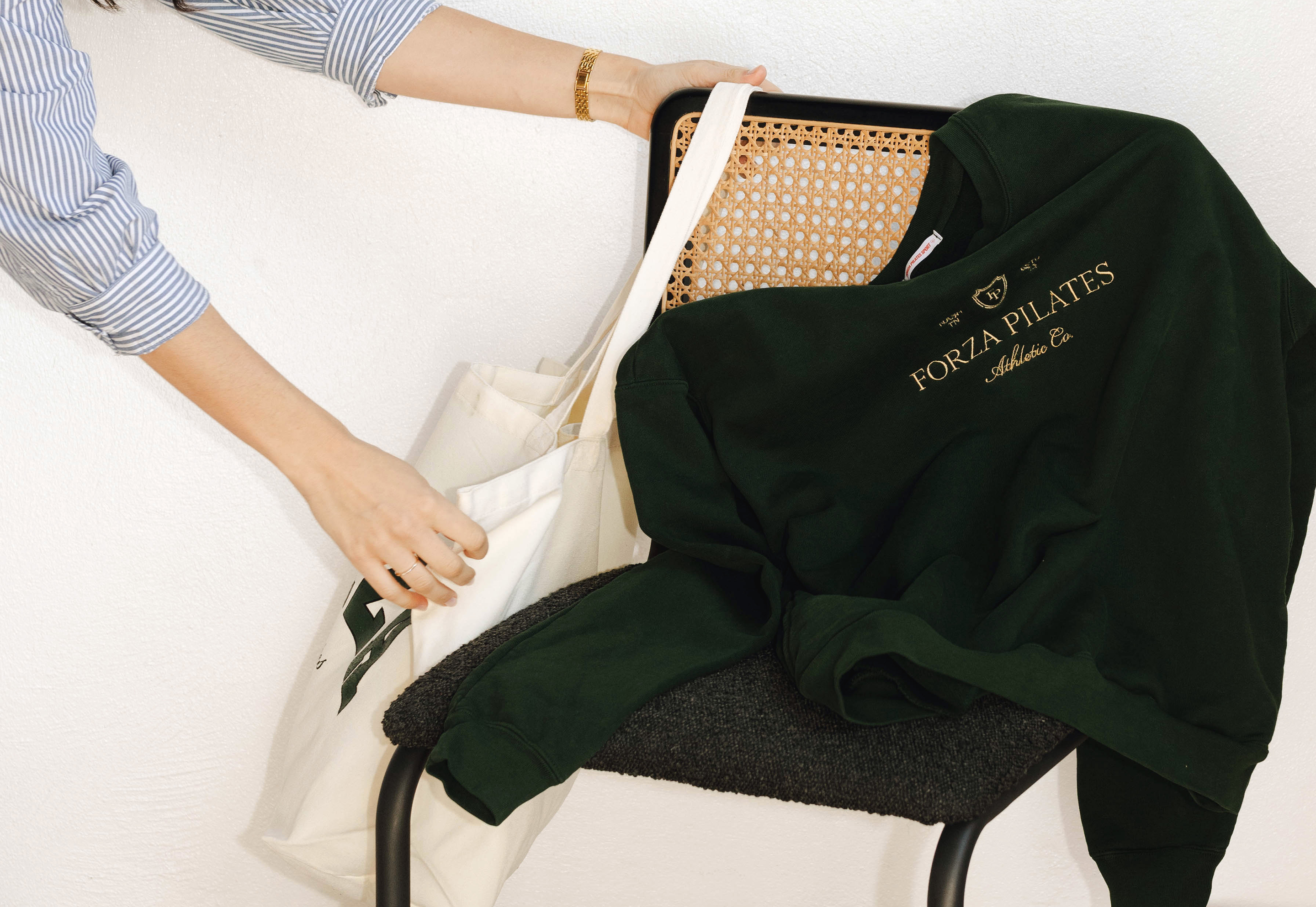 Forza Pilates green sweatshirt and cream tote bag styled on chair, part of street-style merch launch campaign shot on film