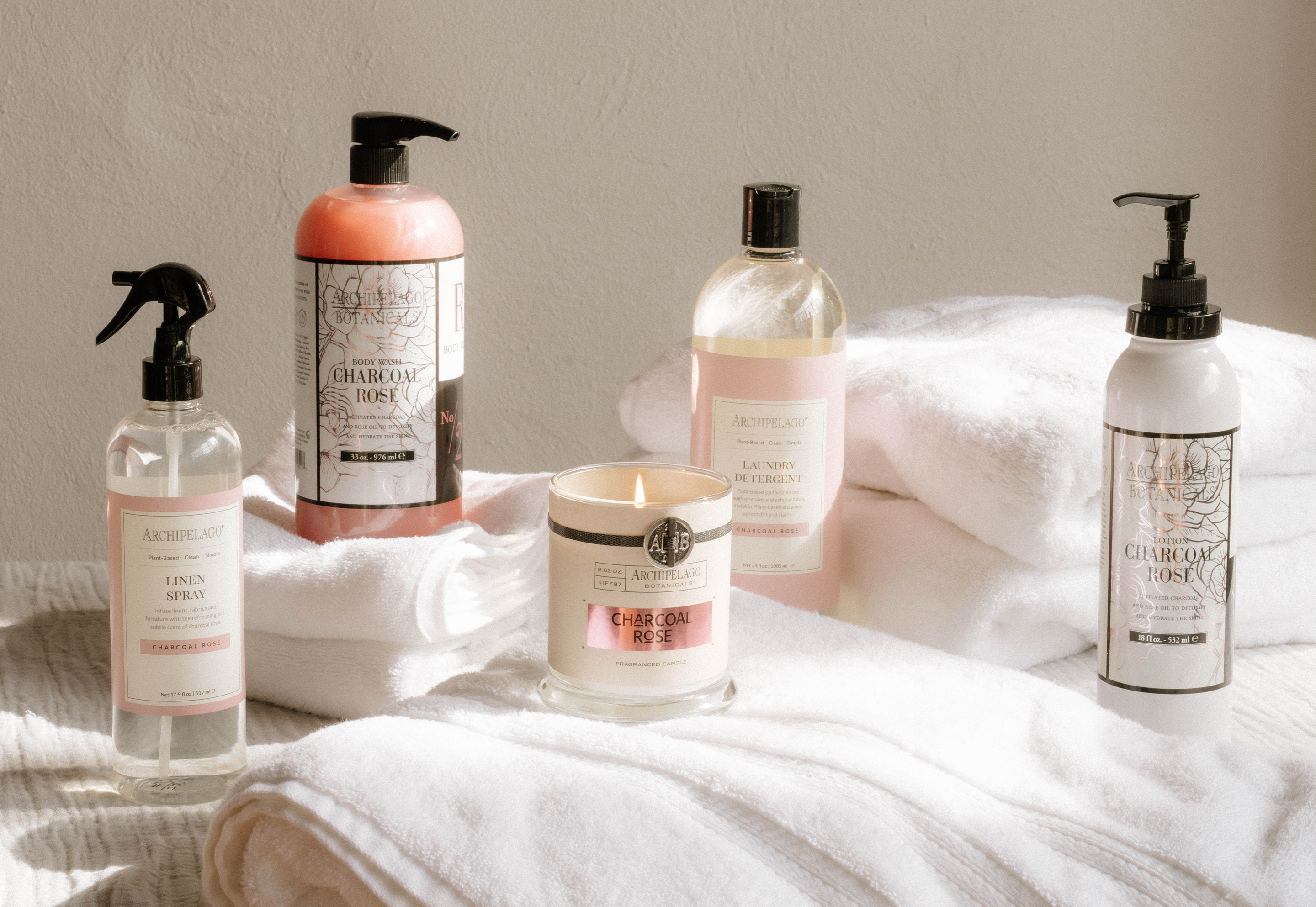 Archipelago Botanicals Charcoal Rose linen spray, body wash, candle, detergent, and lotion with white towels