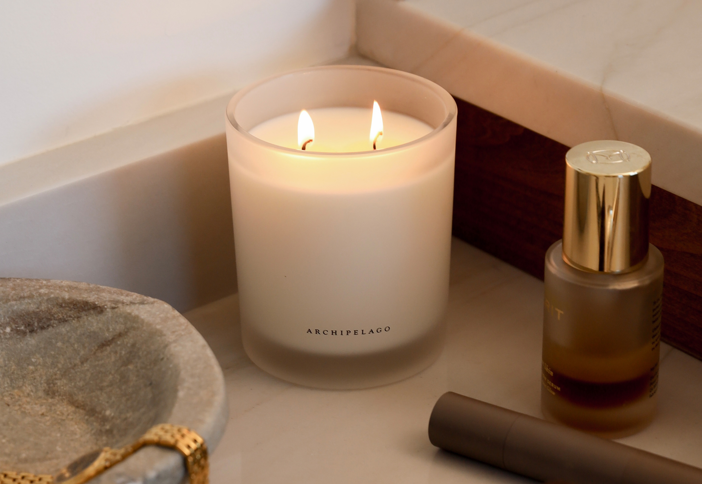 Archipelago Botanicals white frosted glass candle with two flames, styled with luxury skincare bottle and gold-accented perfume – lifestyle product photography by Grain Creative