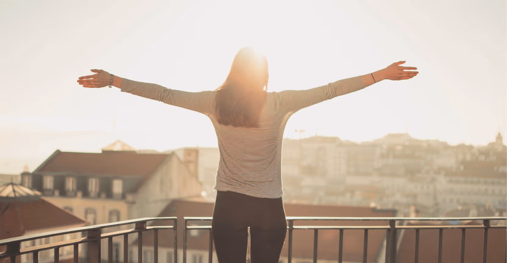 Woman standing on a balcony with open arms at sunrise, symbolizing confidence and new beginnings for women returning to work.
