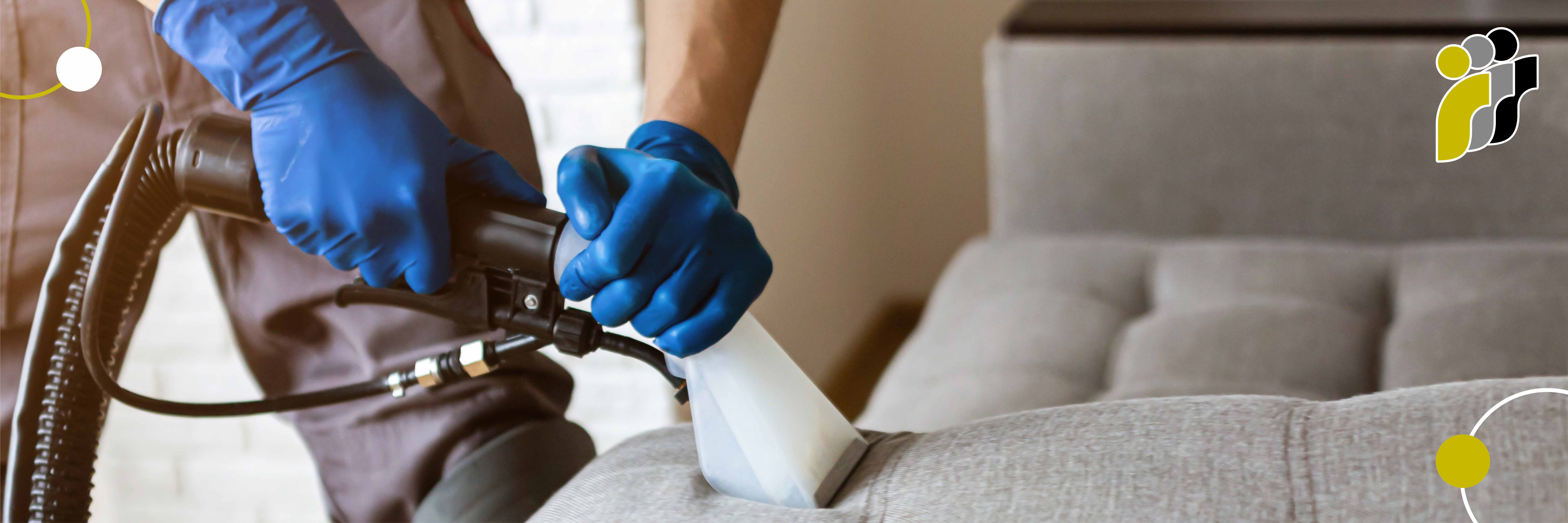 Eine Person mit blauen Handschuhen reinigt ein graues Polstersofa mit einem Dampfreinigungsgerät.