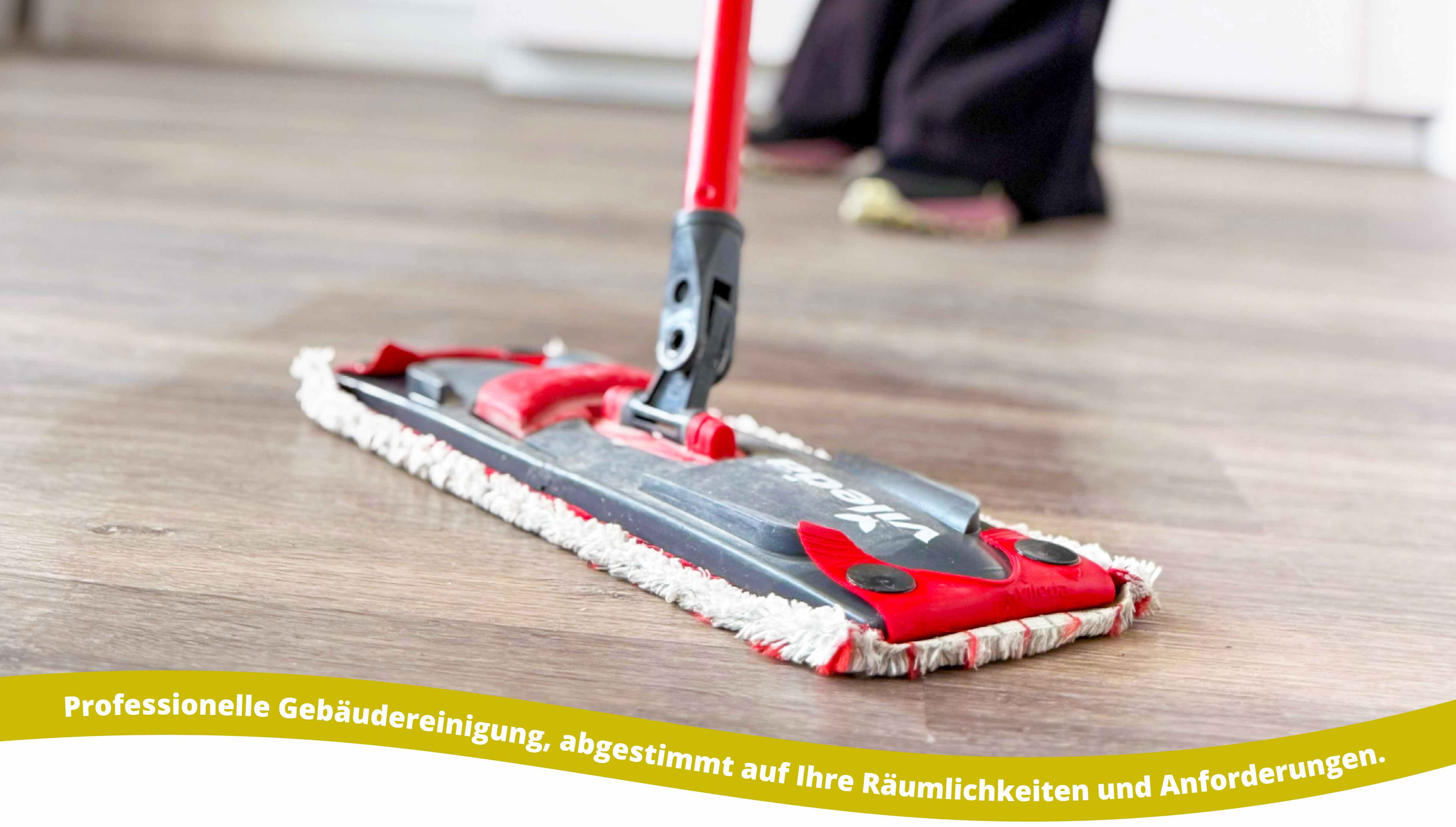 Close-up of a red and black flat mop cleaning a wooden floor, with a person wearing black pants and sneakers in the background.