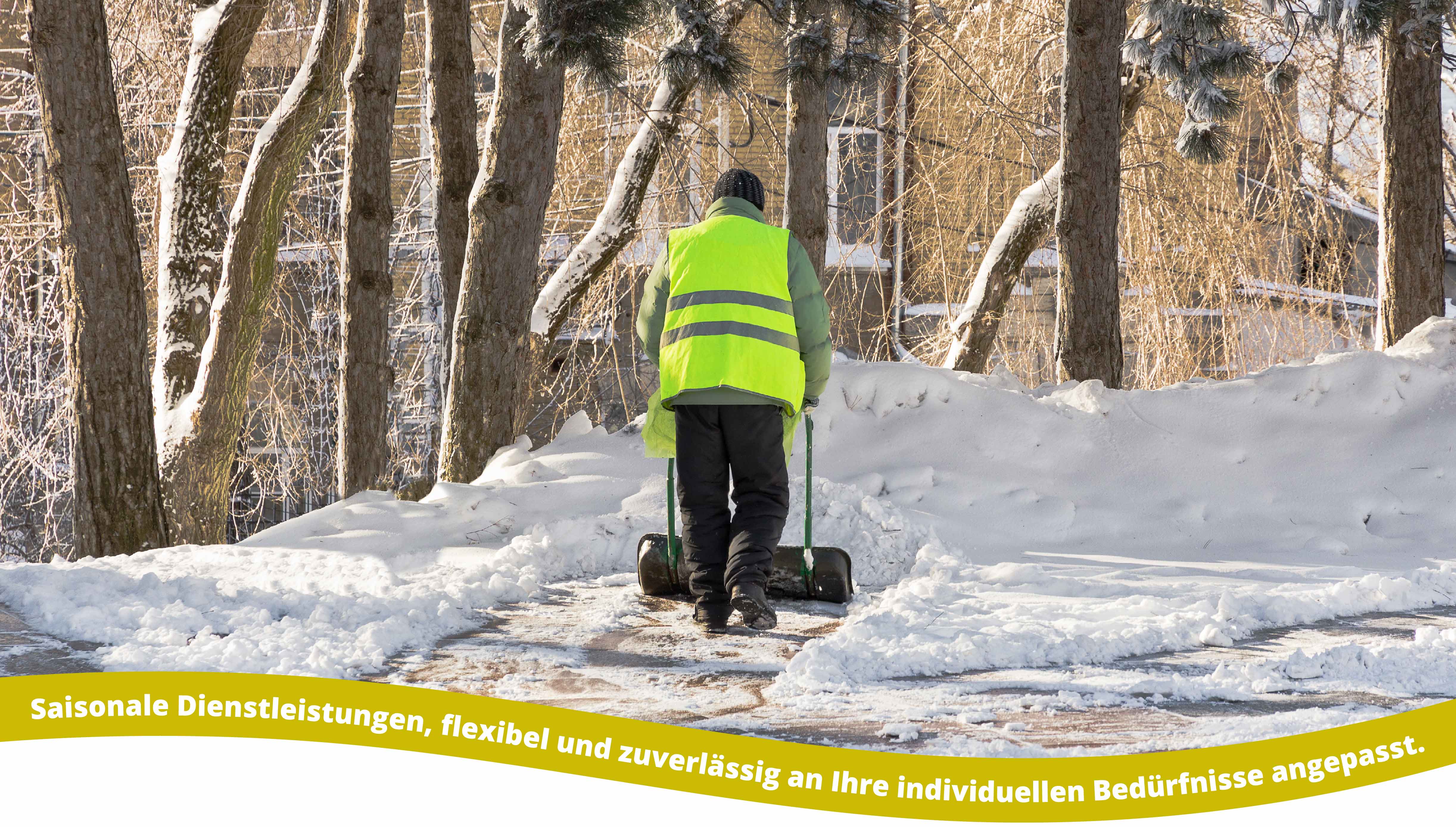 Person wearing a bright yellow reflective vest and black pants shoveling snow on a path surrounded by snow-covered trees and a house in the background.