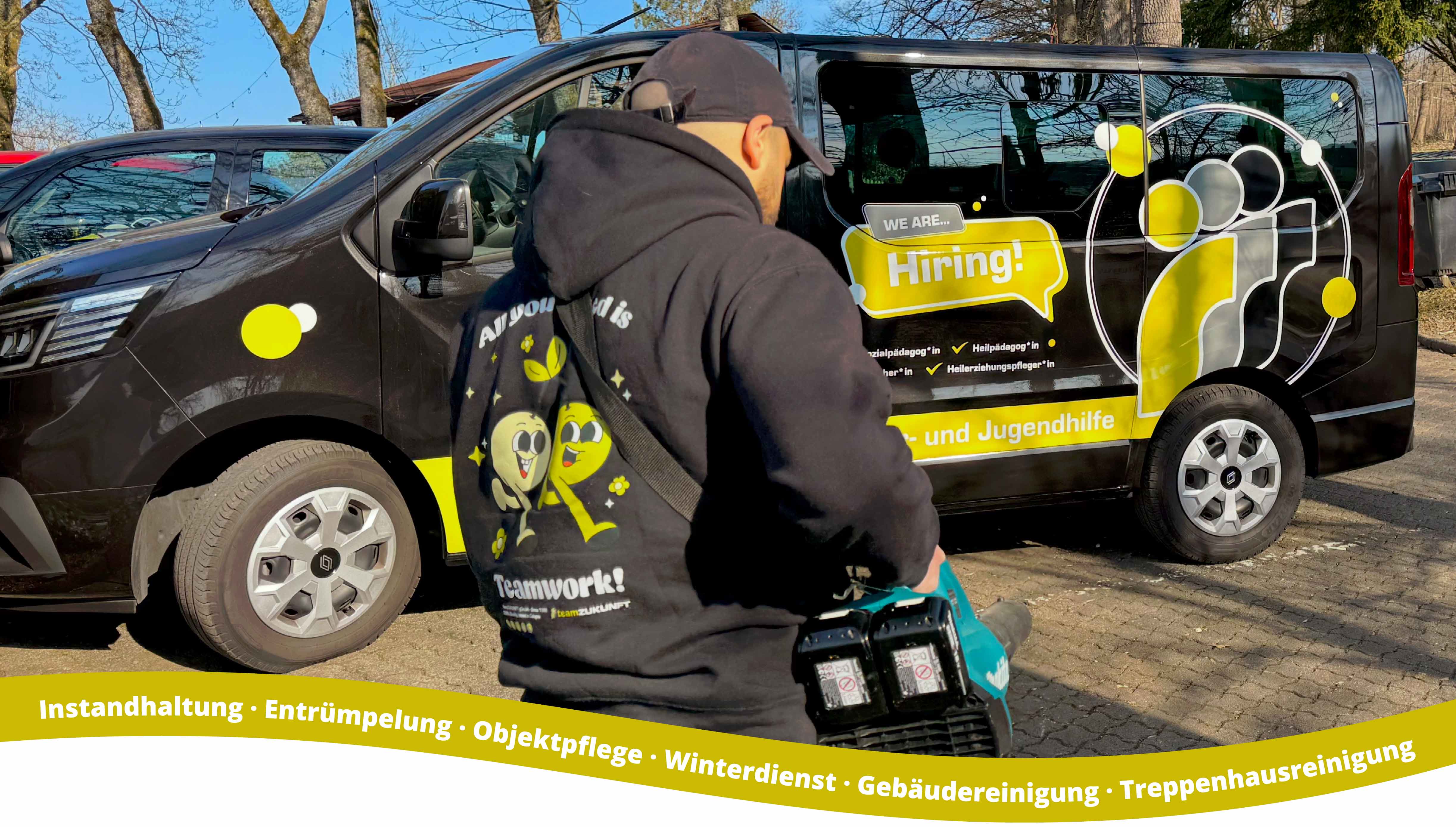 Person in dark hoodie and cap using a leaf blower in front of a black van with yellow and white graphics including text 'We are... Hiring!' and teamSERVICE logo