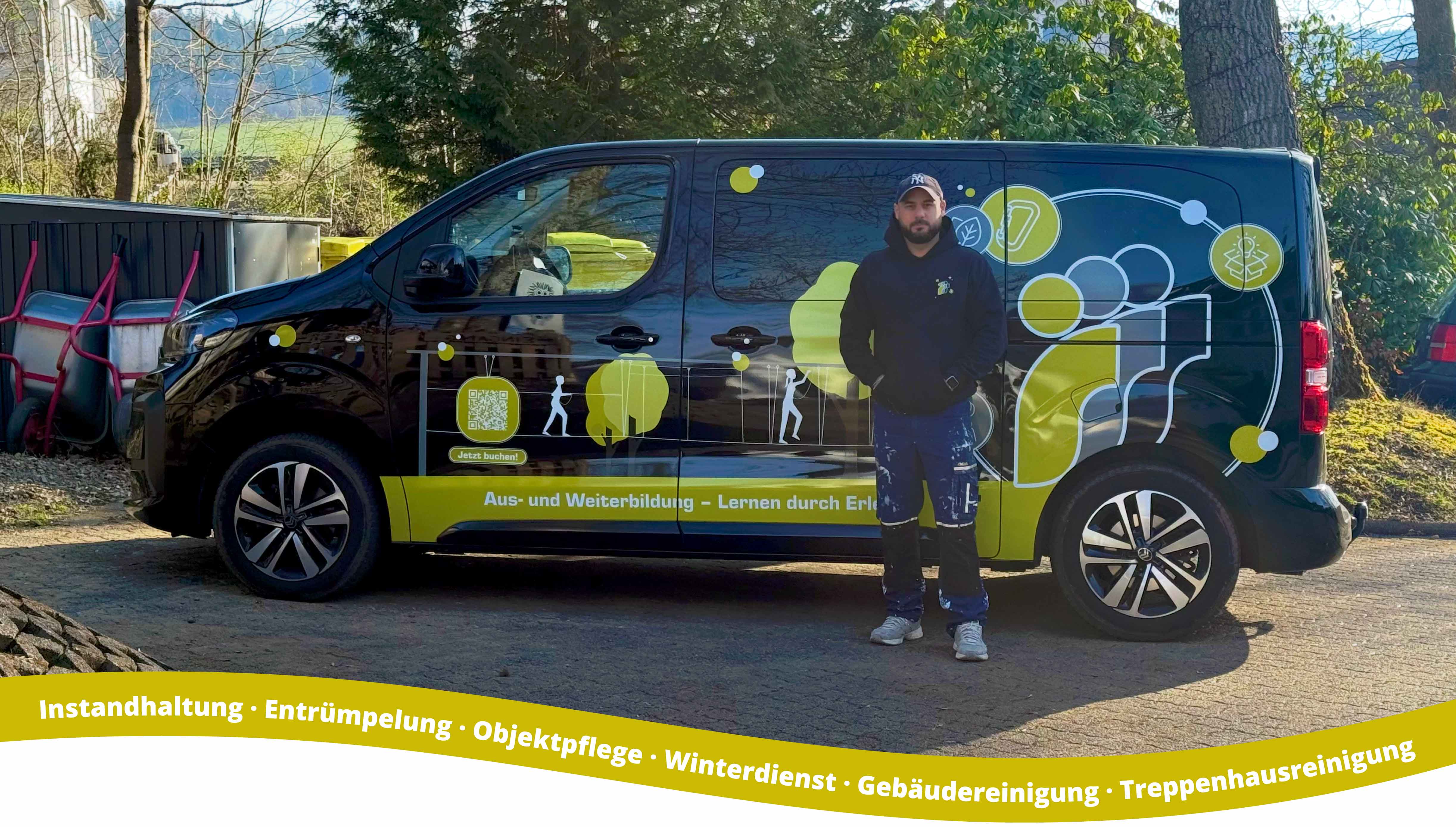 teamSERVICE "Hausmeister" Worker in dark hoodie and blue work pants stands beside a black van with company logo and Contact, parked outdoors near trees and wheelbarrows.