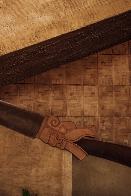 Carved serpent head on the staircase rail against Origen's patterned stone wall