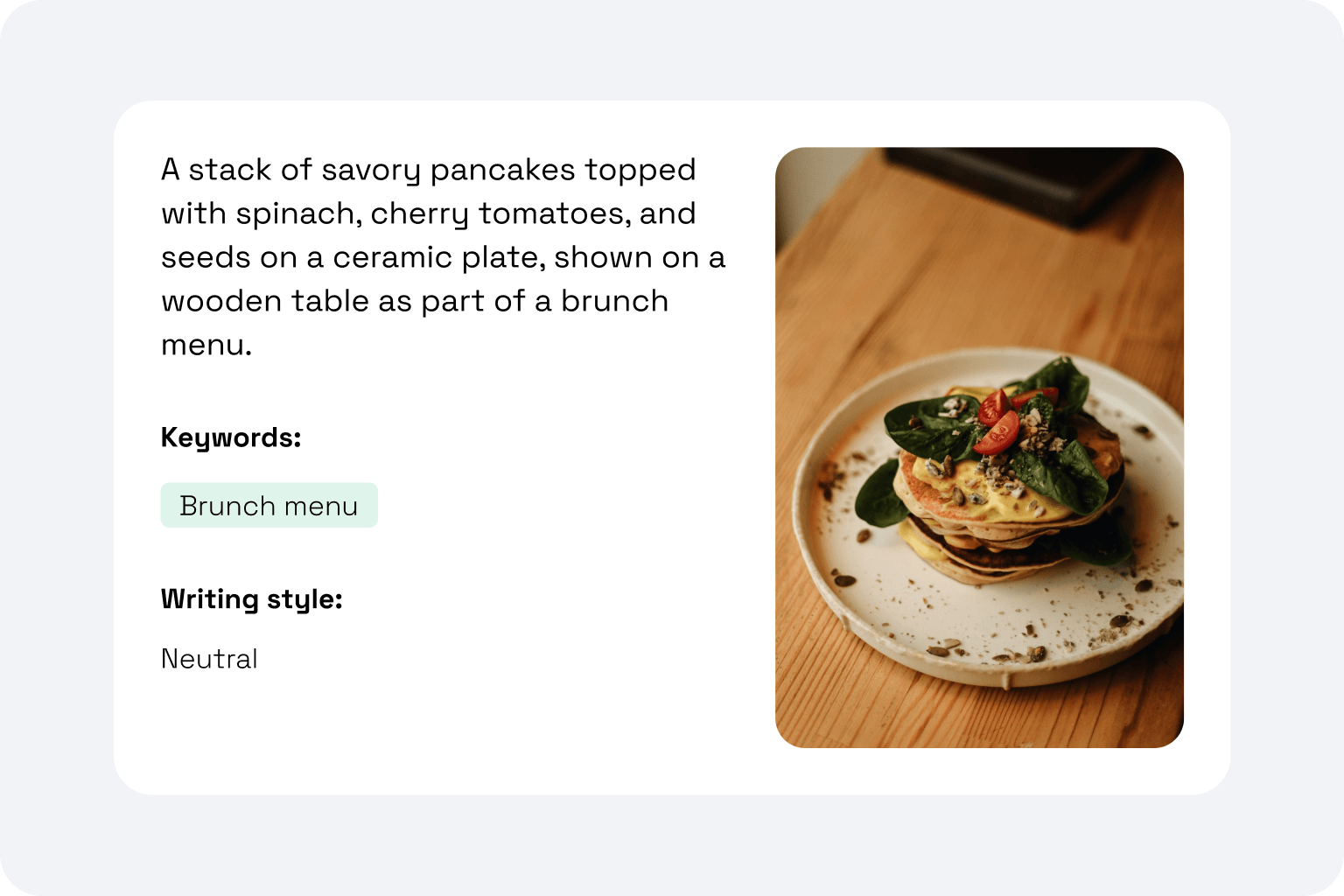 Stack of pancakes with spinach, cherry tomatoes, and seeds on a ceramic plate on a wooden table.