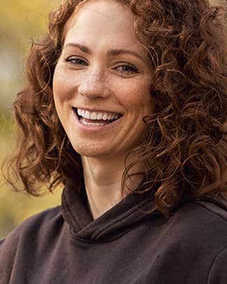 Junge Frau mit lockigem Haar und strahlendem Lächeln – zufriedene Patientin der Q-Zahnärzte Freiburg.