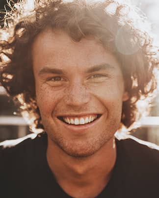 Junger Mann mit natürlichem, strahlendem Lächeln zeigt das Ergebnis moderner ästhetischer Zahnbehandlung bei den Q-Zahnärzten Freiburg.