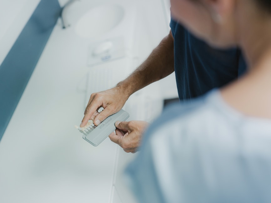 Zahnarzt vergleicht mit einer Farbskala den Zahnfarbton der Patientin vor dem Bleaching – präzise Bestimmung für ein natürliches, helleres Ergebnis.