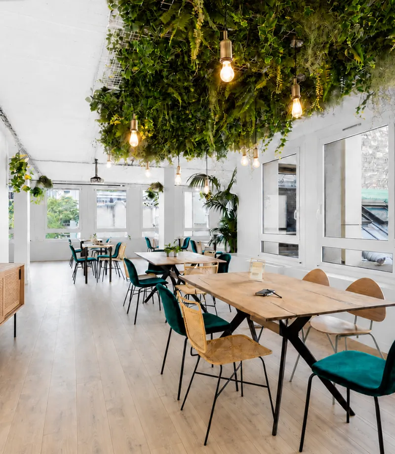 Open space avec tables variées et fausse verdure chez Keeze La Galerie Champs-Élysées, parfait pour une salle de réunion ou un espace de coworking à Paris 8e.
