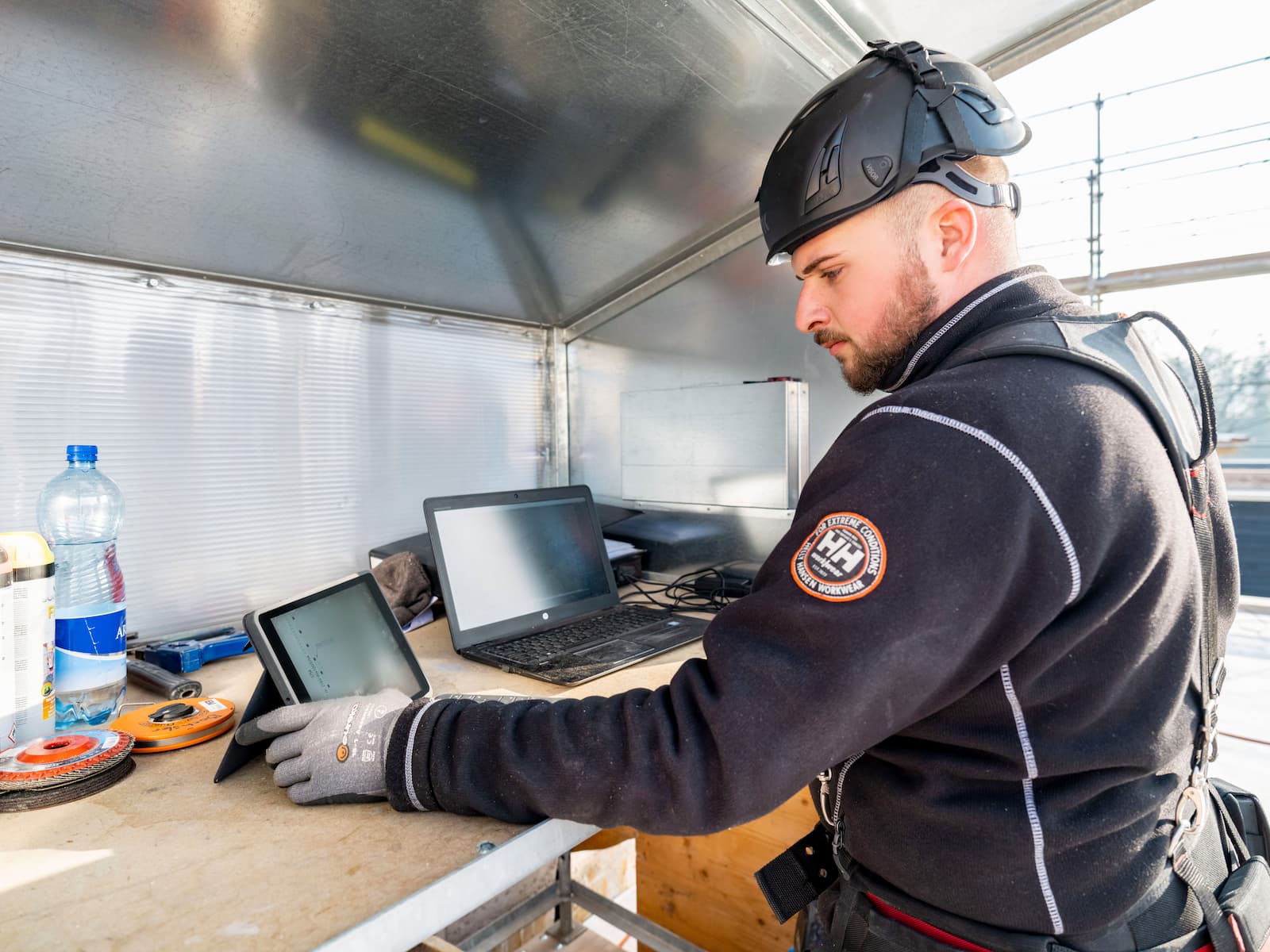 Ein Mitarbeiterder Vögeli Holzbau ist in einem Planhaus beschäftigt mit Notebook und Tablet. Er Studiert die Pläne damit er sein Team informieren kann.