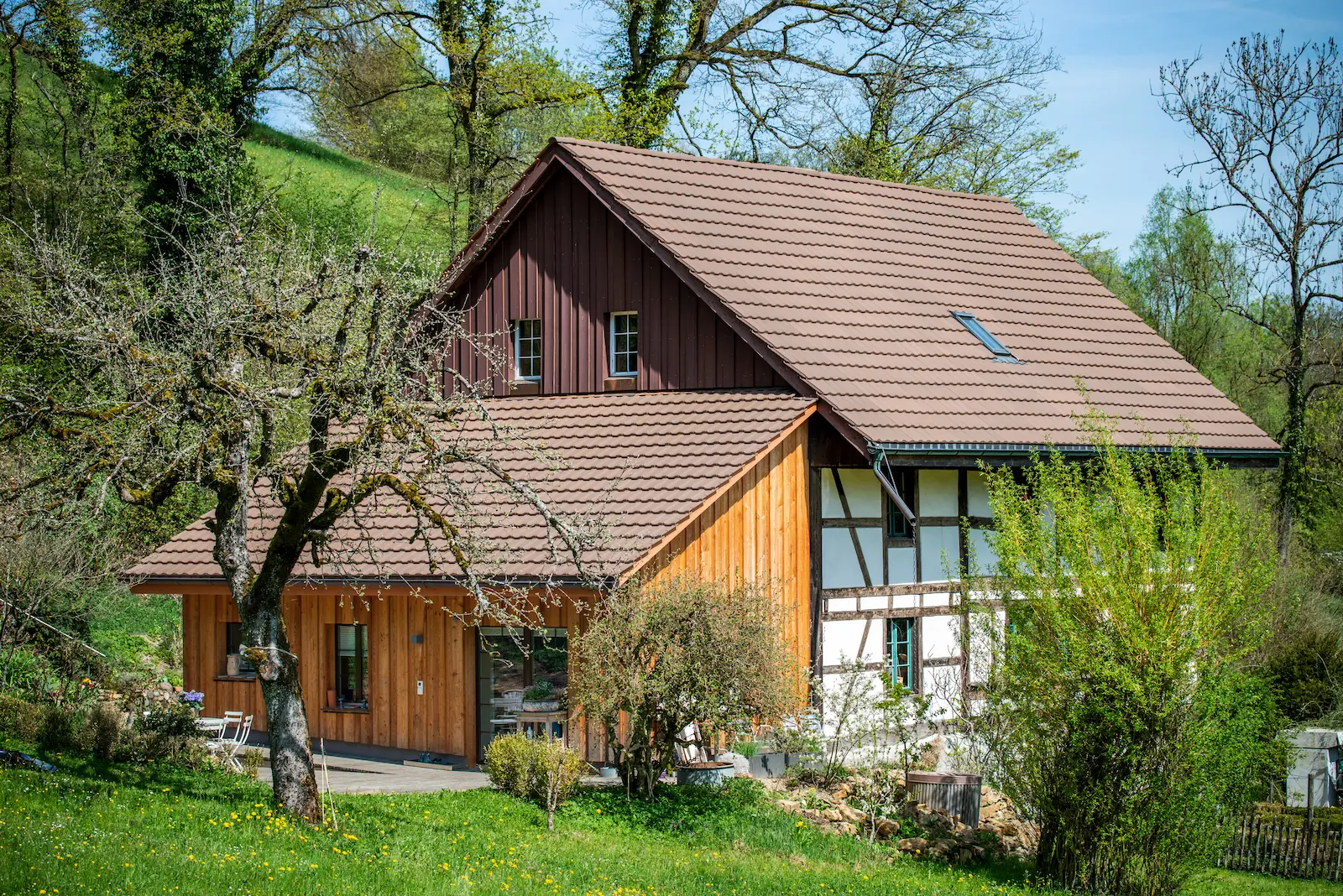 Gesamtansicht eines sanierten Wohnhauses mit Anbau in Holz-Systembau, hinterlüfteter Holzfassade aus Naturschalung und neuem Ziegeldach, Standort Hettenschwil
