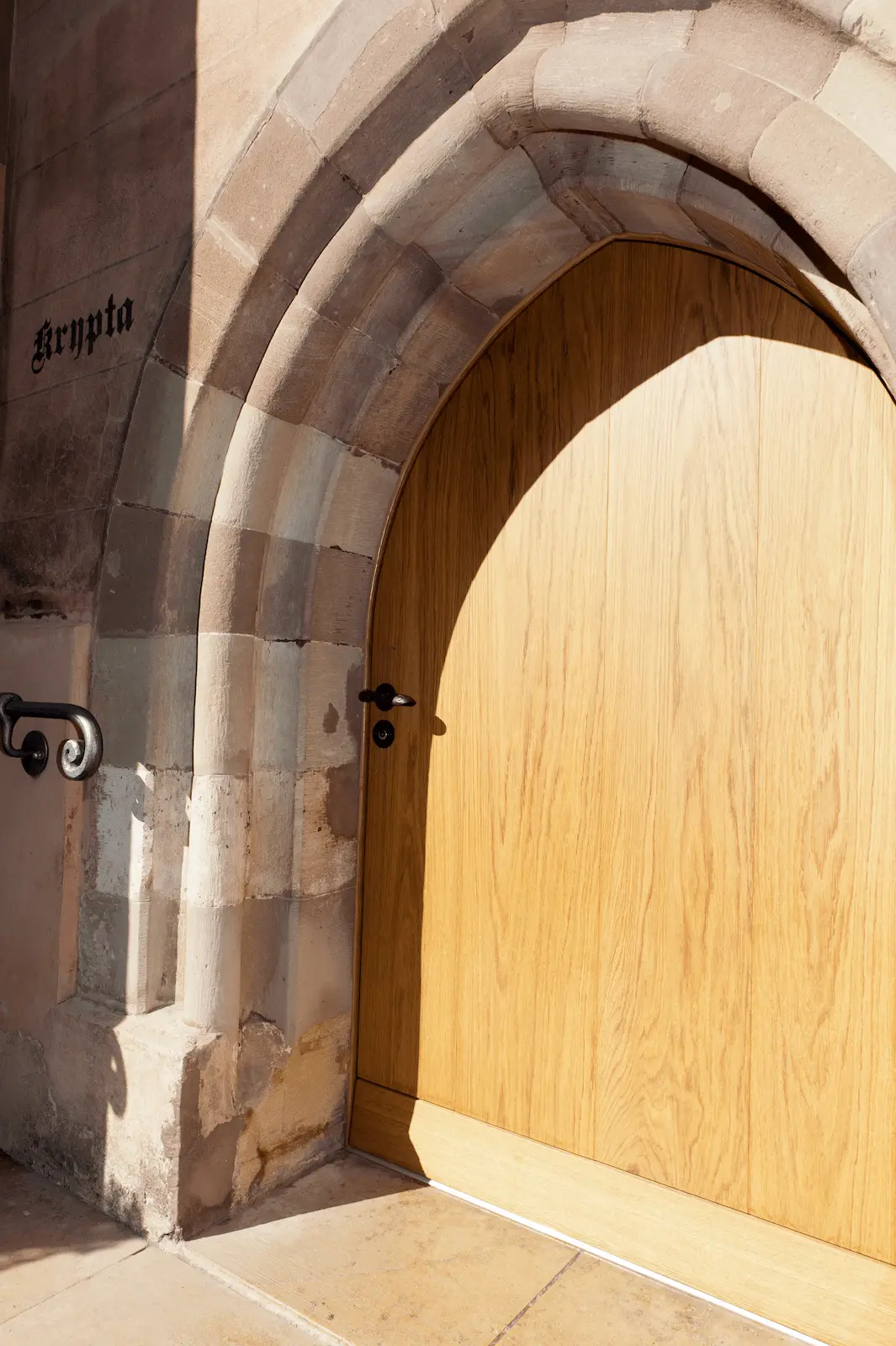 Detailansicht der massiven Eichentüre im Verenamünster Bad Zurzach, eingesetzt in den historischen Sandsteinbogen des Eingangs zur Krypta.