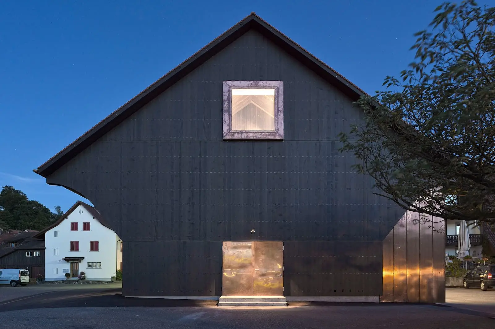 Nachtansicht der Holzfassade mit beleuchtetem Fenster und Kupfertüre am Weingut Würenlingen