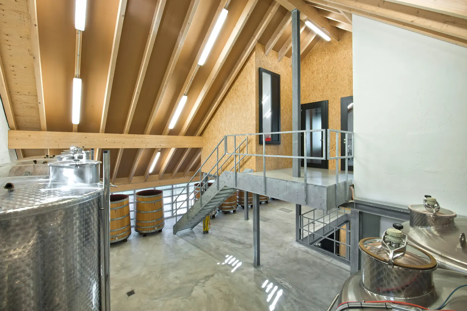 Sichtbare Holzkonstruktion des Dachstuhls über Produktionsbereich mit Edelstahltanks im Weingut Würenlingen