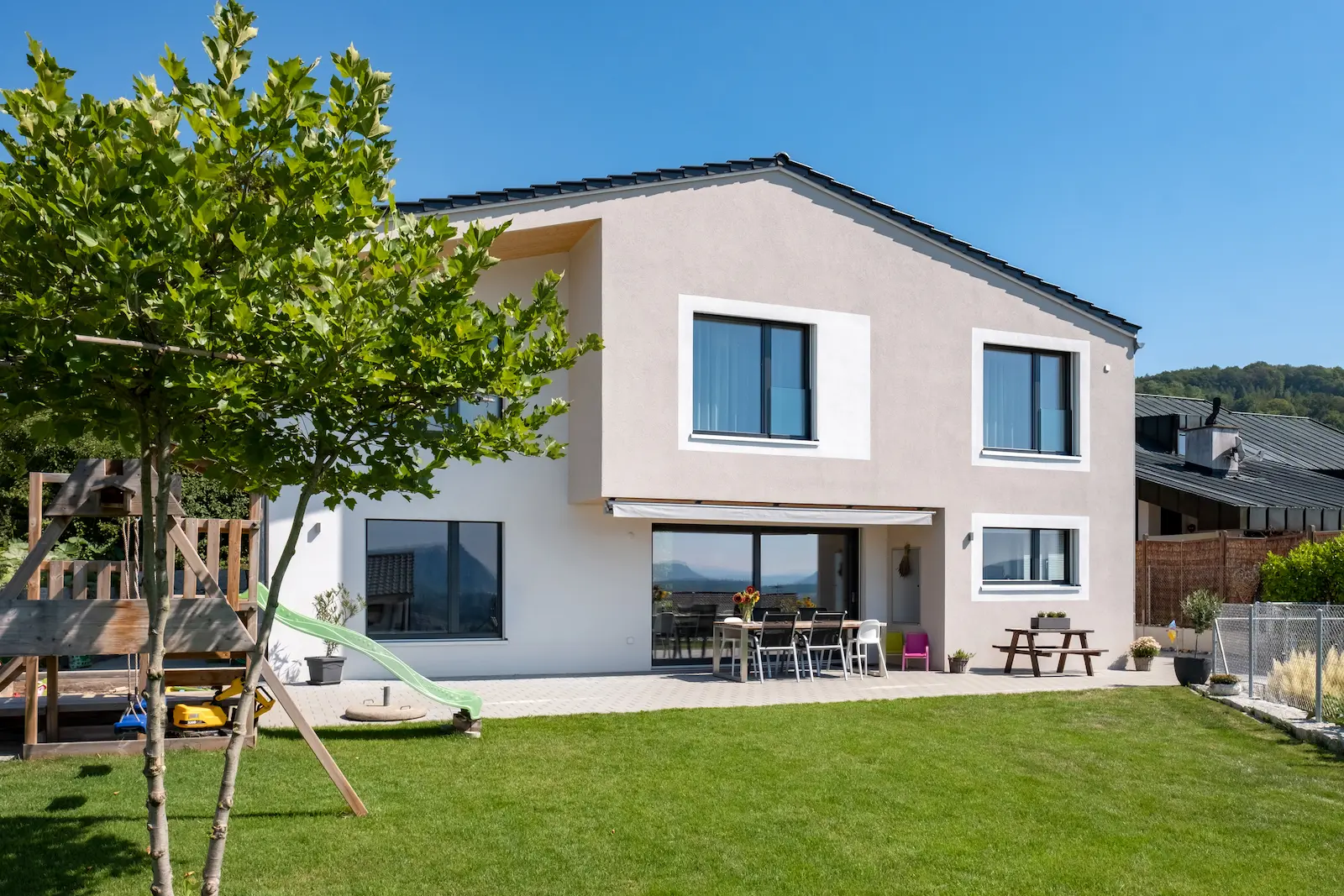 Einfamilienhaus in Klingnau mit moderner Fassade, Sichtdach aus Holz, Velux-Fenstern und überdachtem Sitzplatz im Garten.