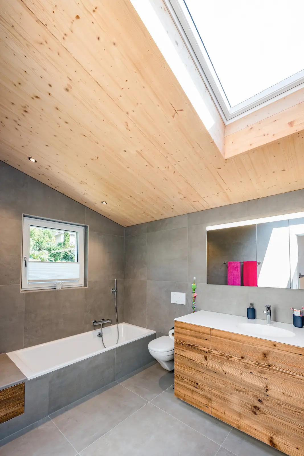 Modernes Bad mit Dachfenster, sichtbarer Holzdecke und Waschtisch aus Altholz im Einfamilienhaus in Holzelementbauweise in Klingnau.
