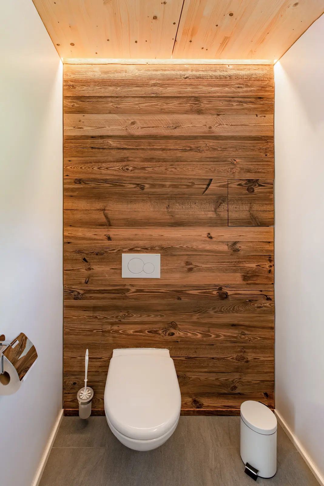 Stimmiges WC mit Rückwand aus Altholz und indirekter Beleuchtung – Innenausbau mit natürlichen Materialien und modernem Lichtkonzept.