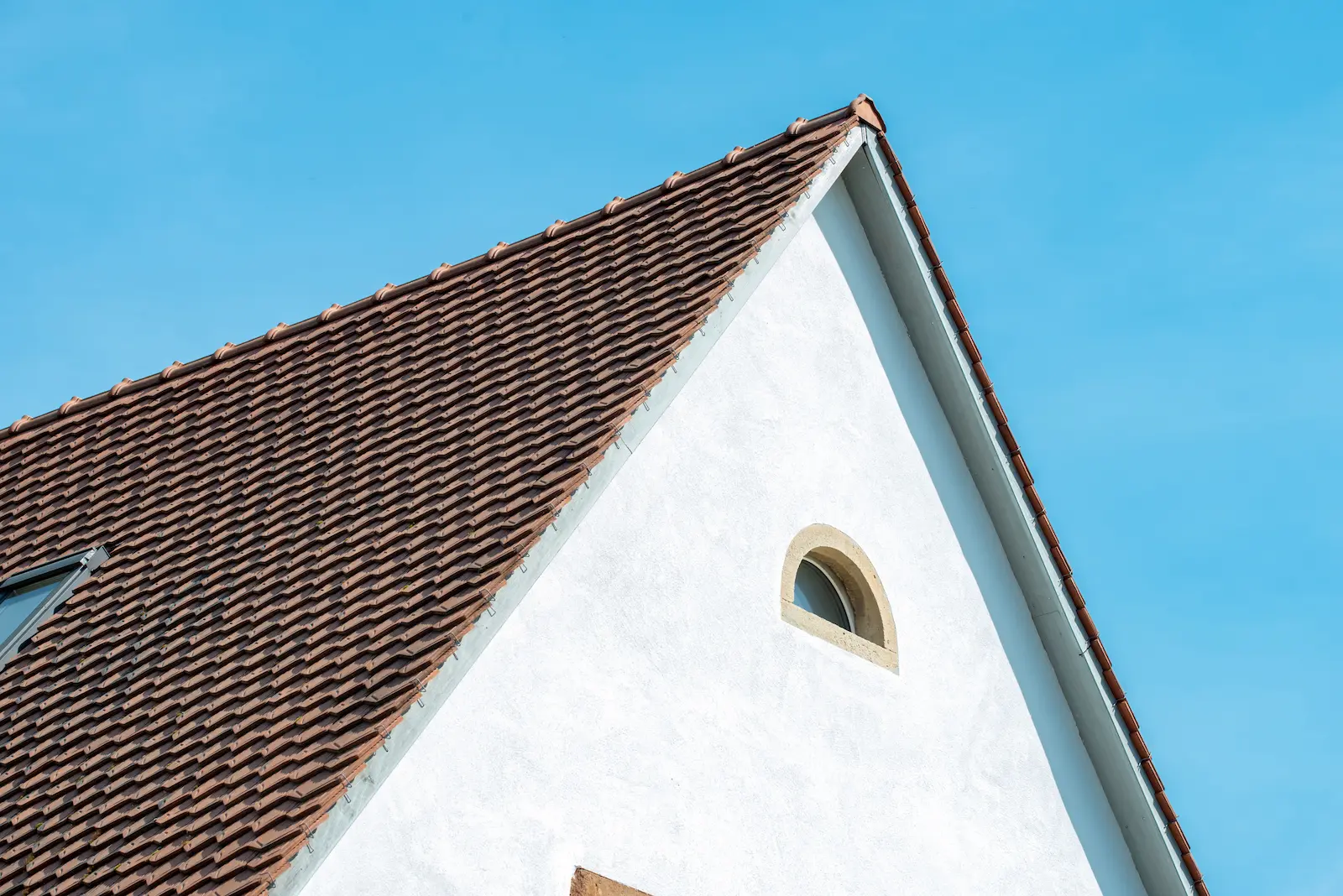Alt-Text: Detailansicht der neuen Bedachung in Hottwil mit Biberschwanzziegeln und verputztem Giebel mit Rundfenster.