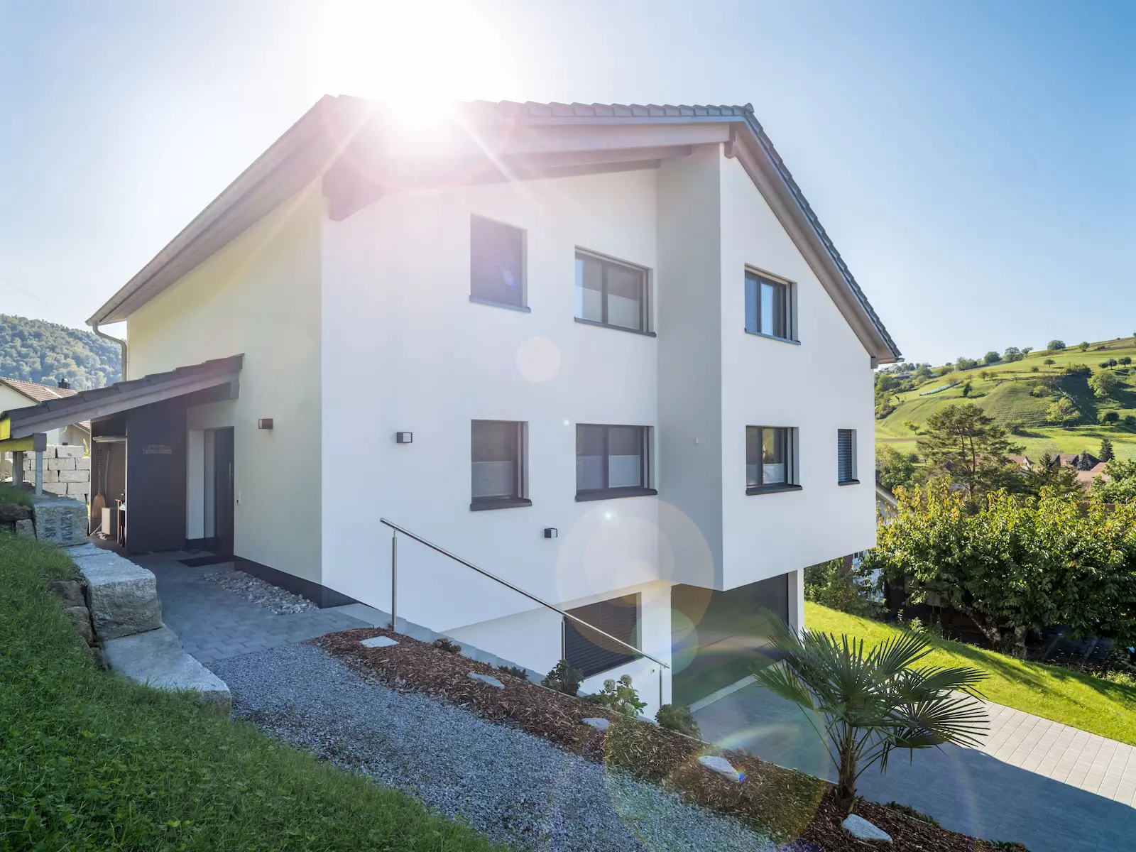 Aussenansicht mit grossen Fenstern, Holzelementwänden und einfallendem Sonnenlicht