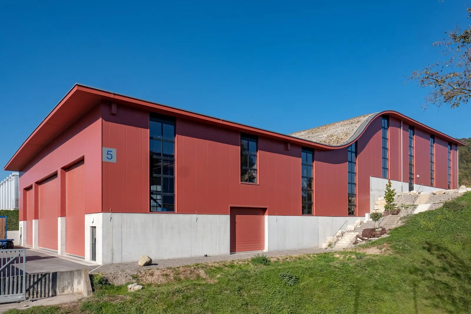 Aussenansicht Hallenbau mit roter Fassadenverkleidung und grossen Fenstern