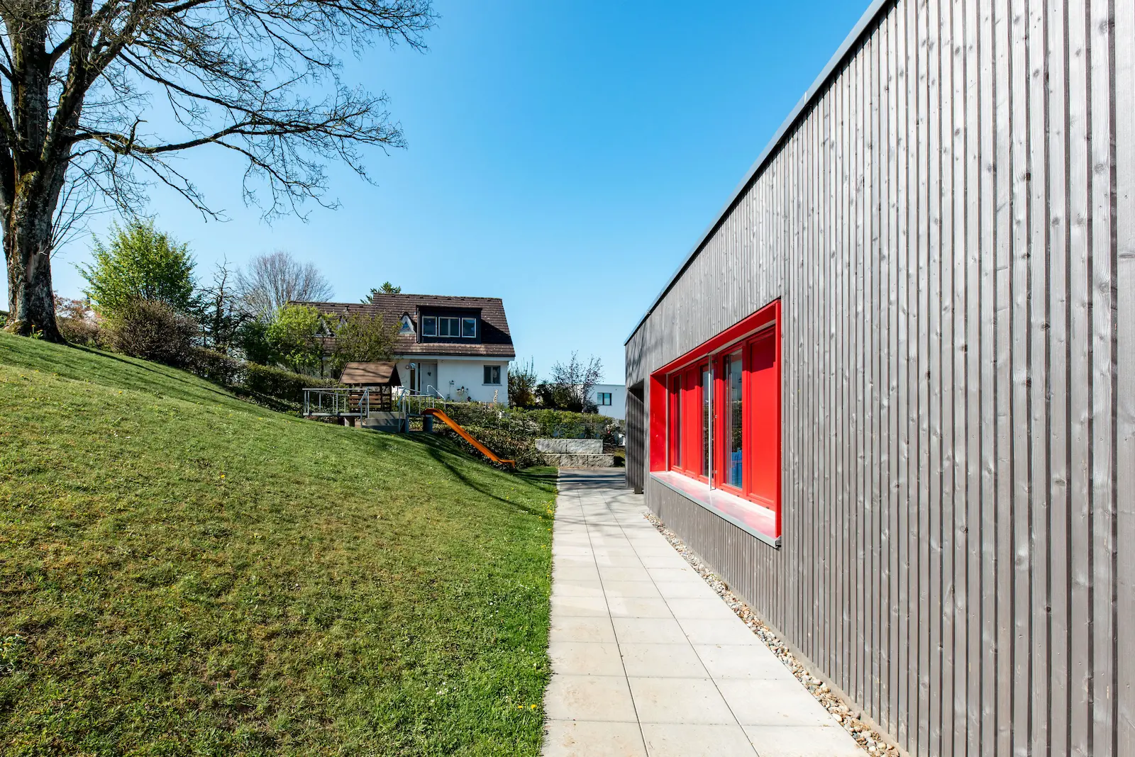Längsansicht Fassade mit roten Fensterbändern.