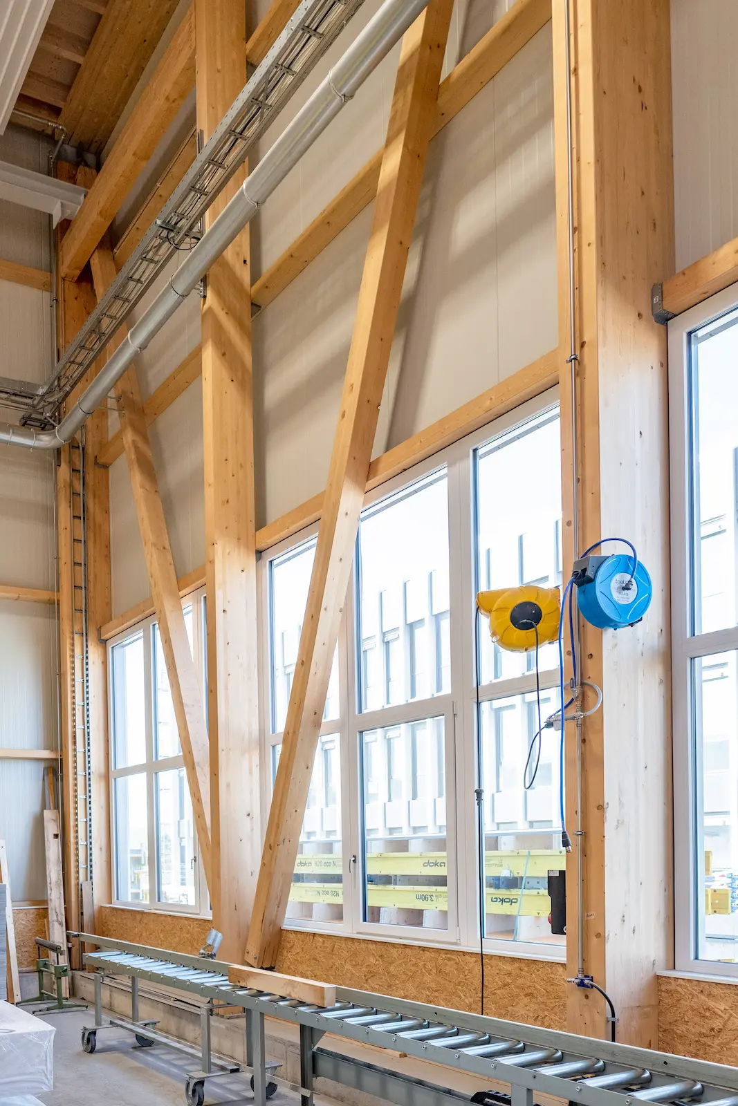 Detailansicht einer Aussenwand mit Holztragwerk und diagonalen Verstrebungen neben Fensterfront