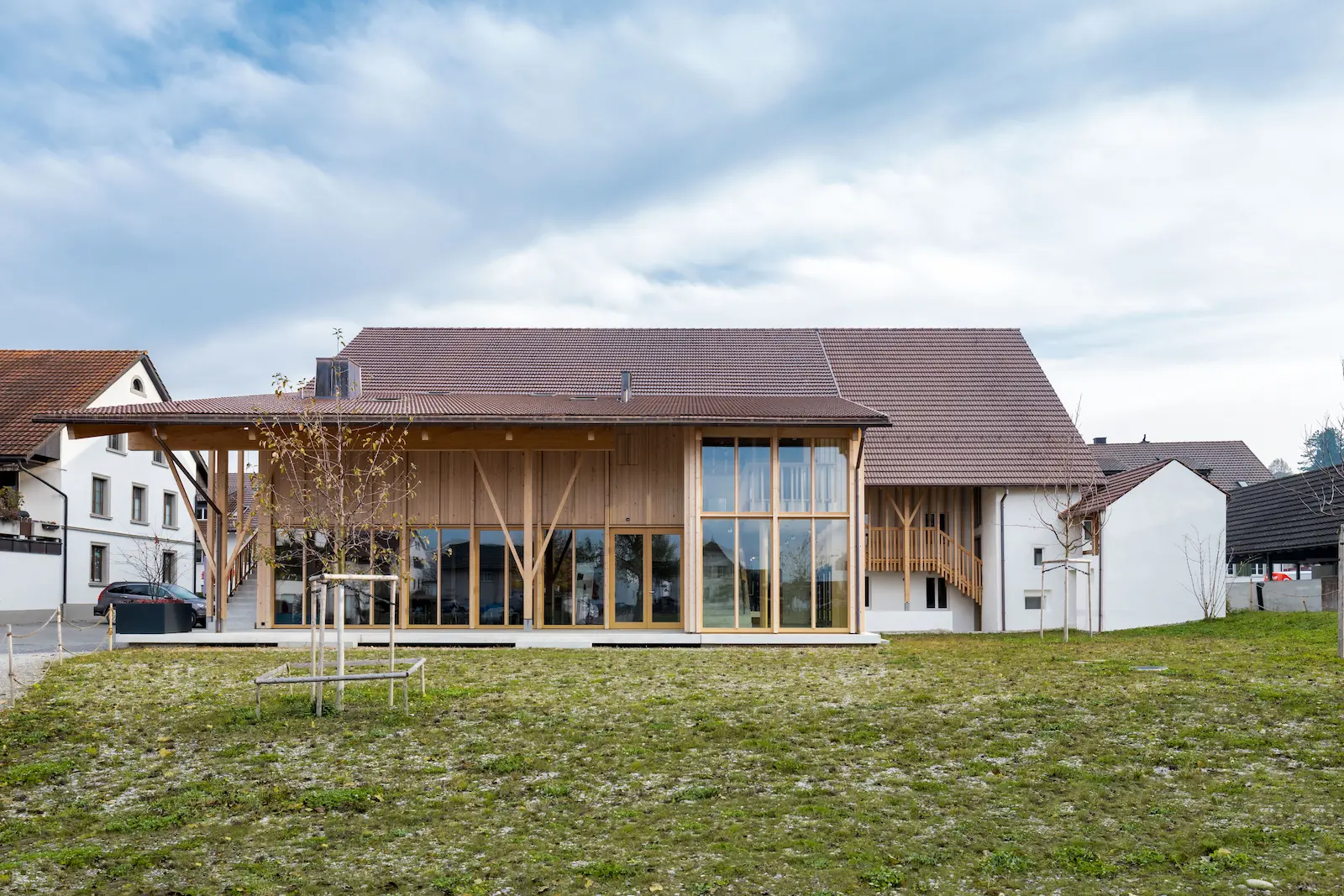 Gesamtansicht mit Glasfassade, Holzstützen und Ziegeldach