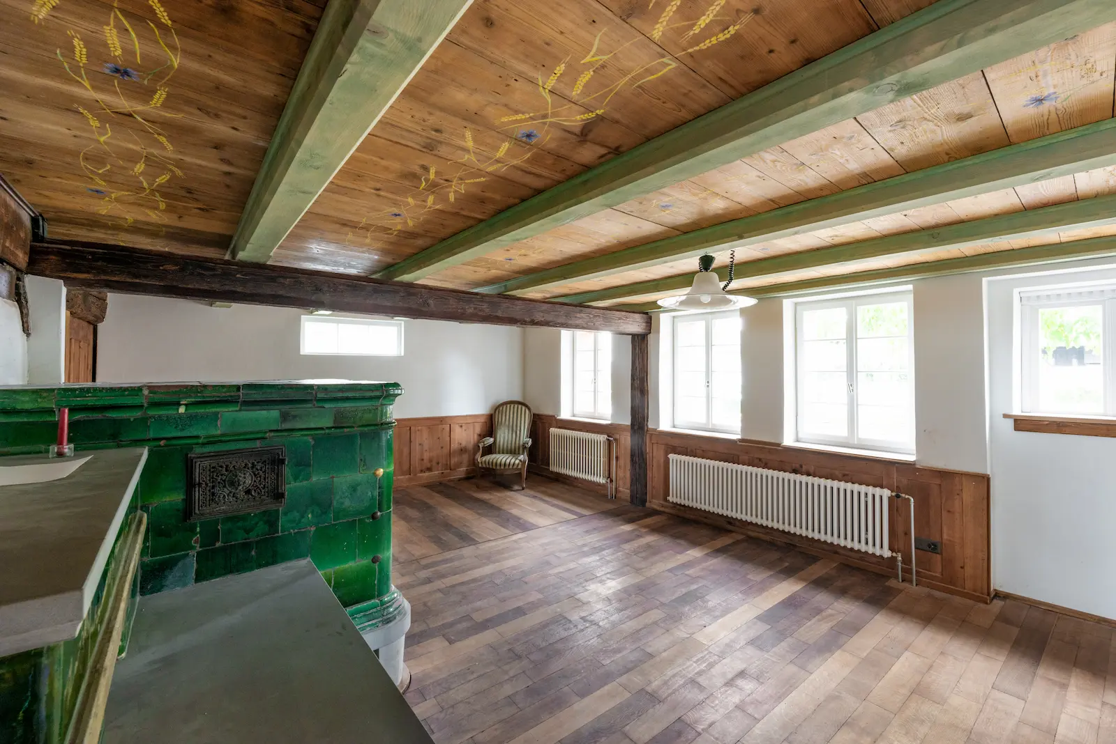 Wohnraum mit restauriertem Holzboden, grünem Kachelofen und bemalter Decke im Dalihaus Hausen