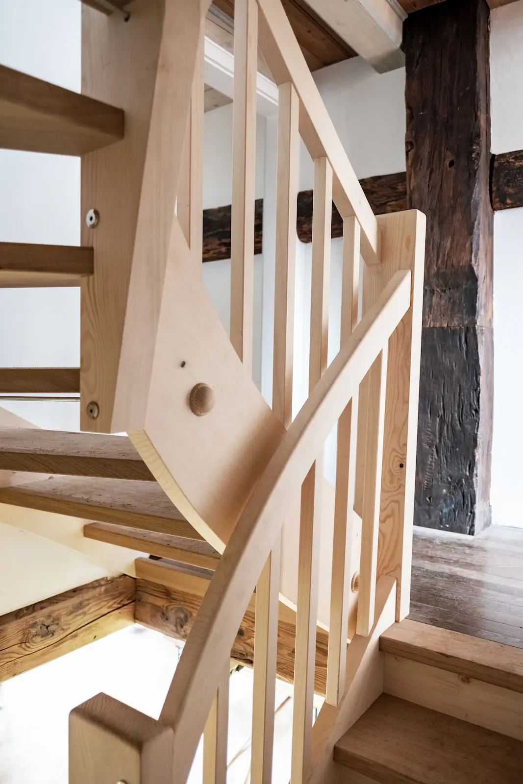 Handwerklich gefertigte Treppe im Dahlihaus mit harmonischer Verbindung zu historischen Balken.