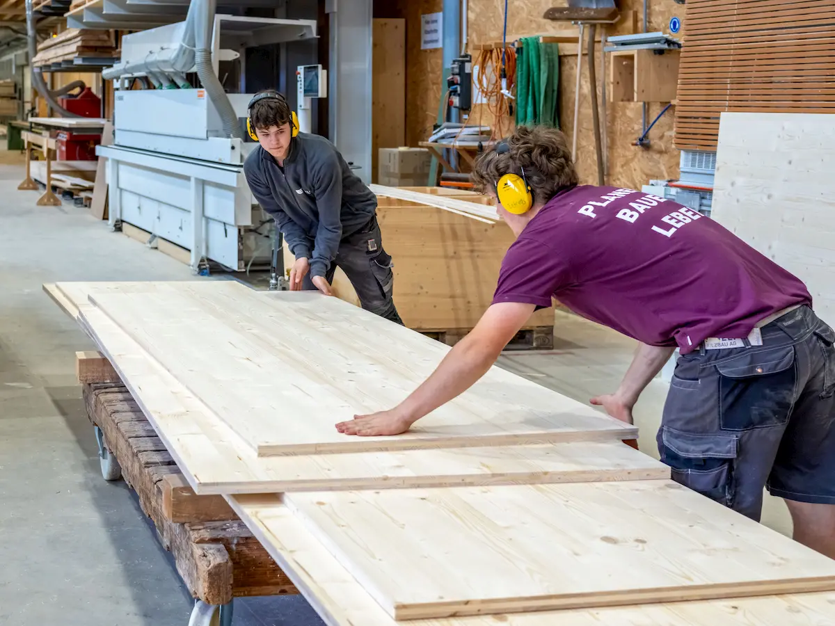 Ein Mitarbeiter der Vögeli Holzbau ist mit einer grossen Holzplatte beschäftigt. Er packt diese auf einen Plattenwagen.