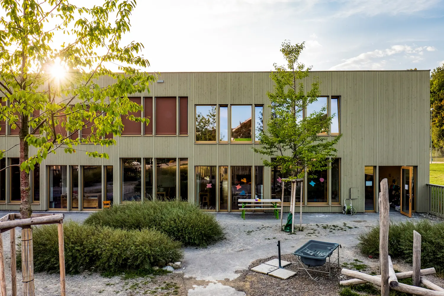 Fassade eines Neubaus mit Bäumen und Garten während einem Sonnenuntergang