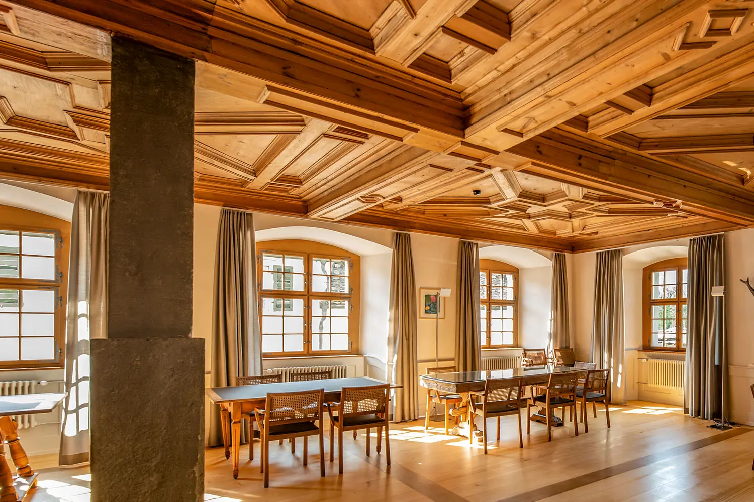 Historischer Raum mit kunstvoller Holzdecke und großen Fenstern – meisterhaft restaurierte Innenarchitektur mit Charme.