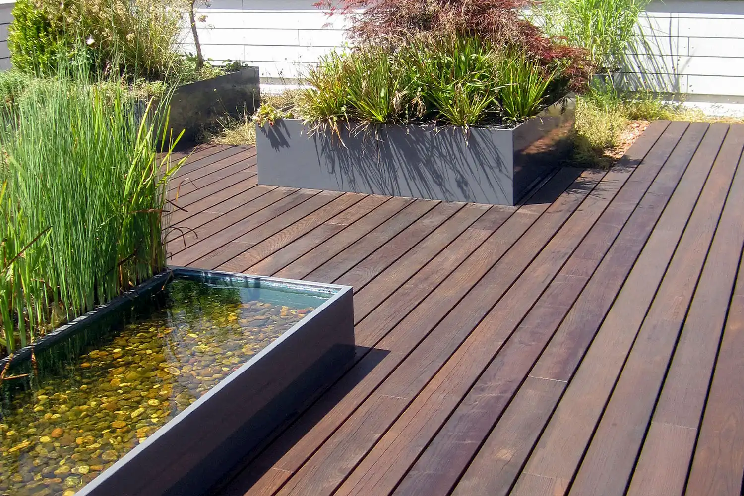 Holzterrasse mit Wasserbecken und Pflanztrögen – natürliche Gestaltung für stilvolle Aussenräume.