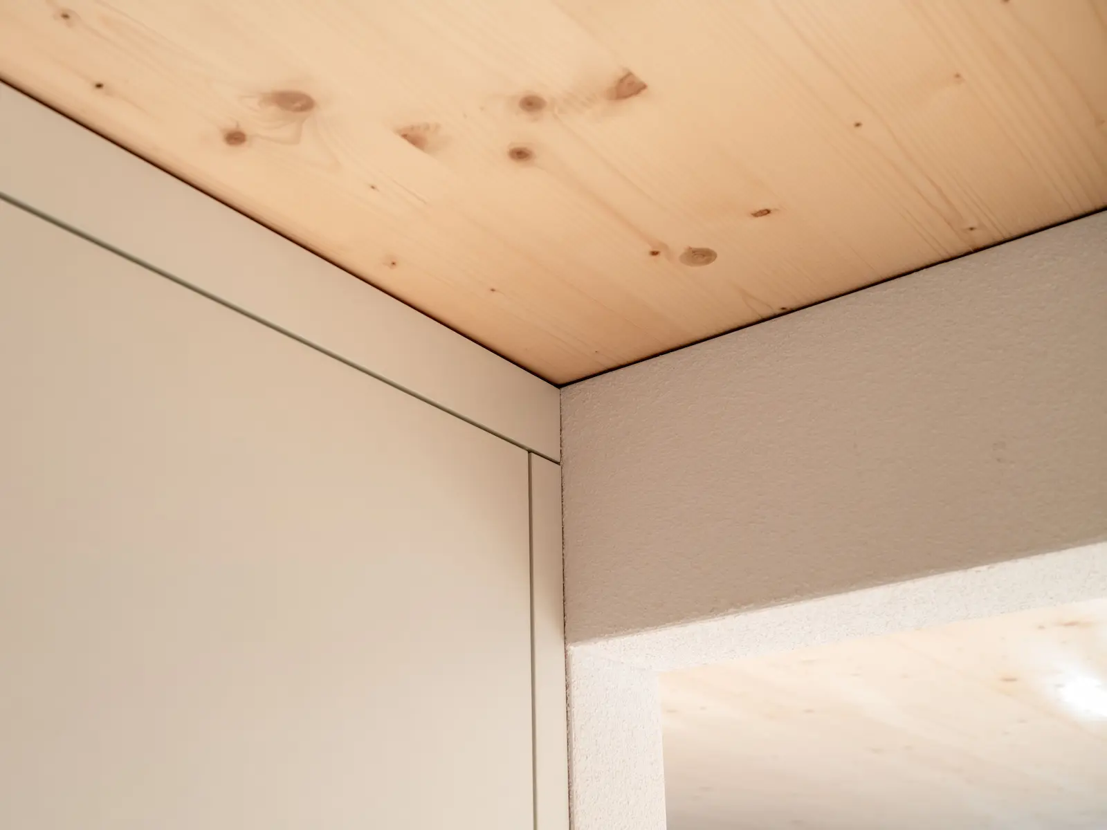 Sauber ausgeführter Anschluss zwischen Wandverkleidung und Holzdecke im Innenausbau des Mehrfamilienhauses Obstgarten.