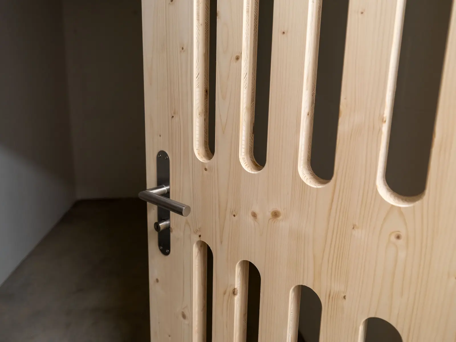 Detailaufnahme einer Kellerabteil-Tür aus Holz mit präzise gefrästen Lüftungsschlitzen und Edelstahlgriff Obstgarten Würenlingen