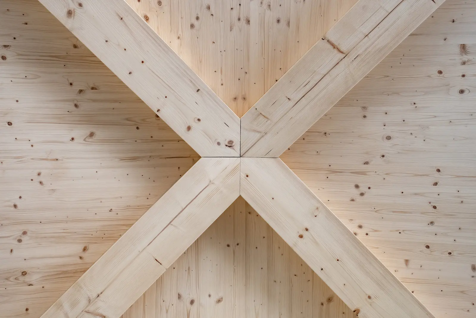 Sichtbare Holzkonstruktion eines Zeltdachs mit sich kreuzenden Gratsparren aus Brettschichtholz und sauber gearbeiteten Fugen