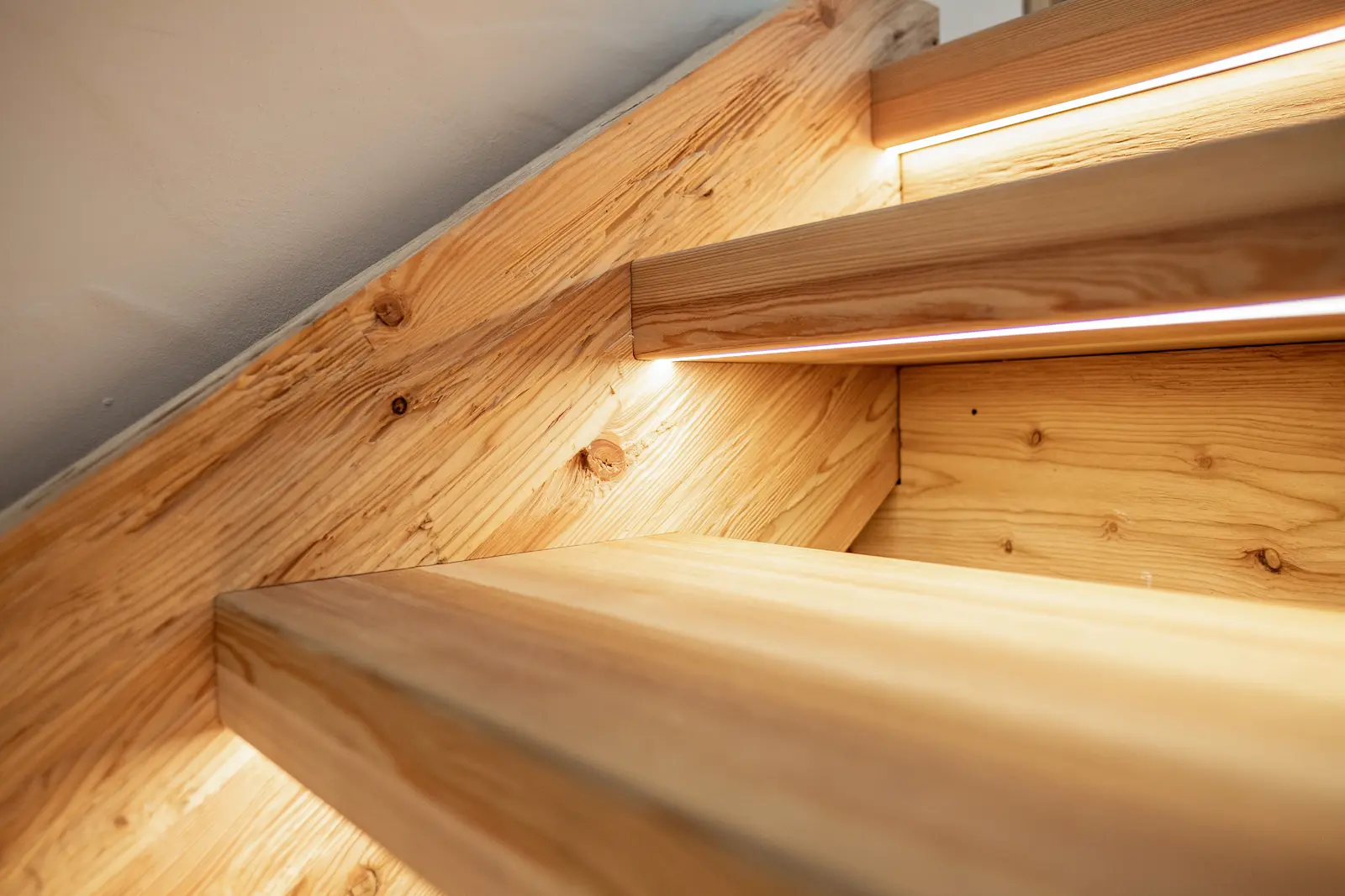 Detailaufnahme der Lärchenstufen mit präzise eingelassenen LED-Bändern und feiner Maserung des massiven Holzes.