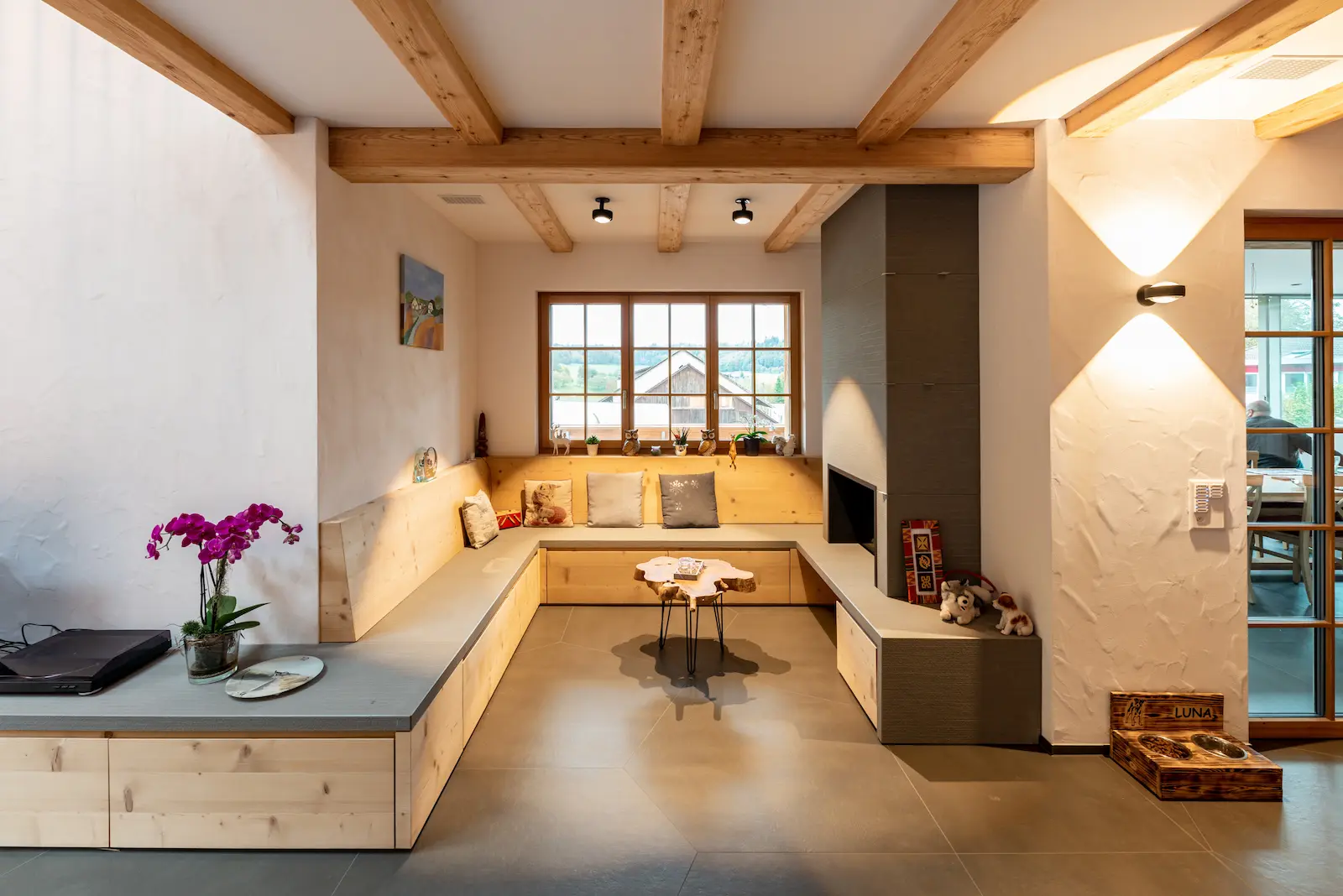 Eckbank im Wohnraum mit durchlaufender Rückenlehne, Massivholzverkleidung und Steinauflage.