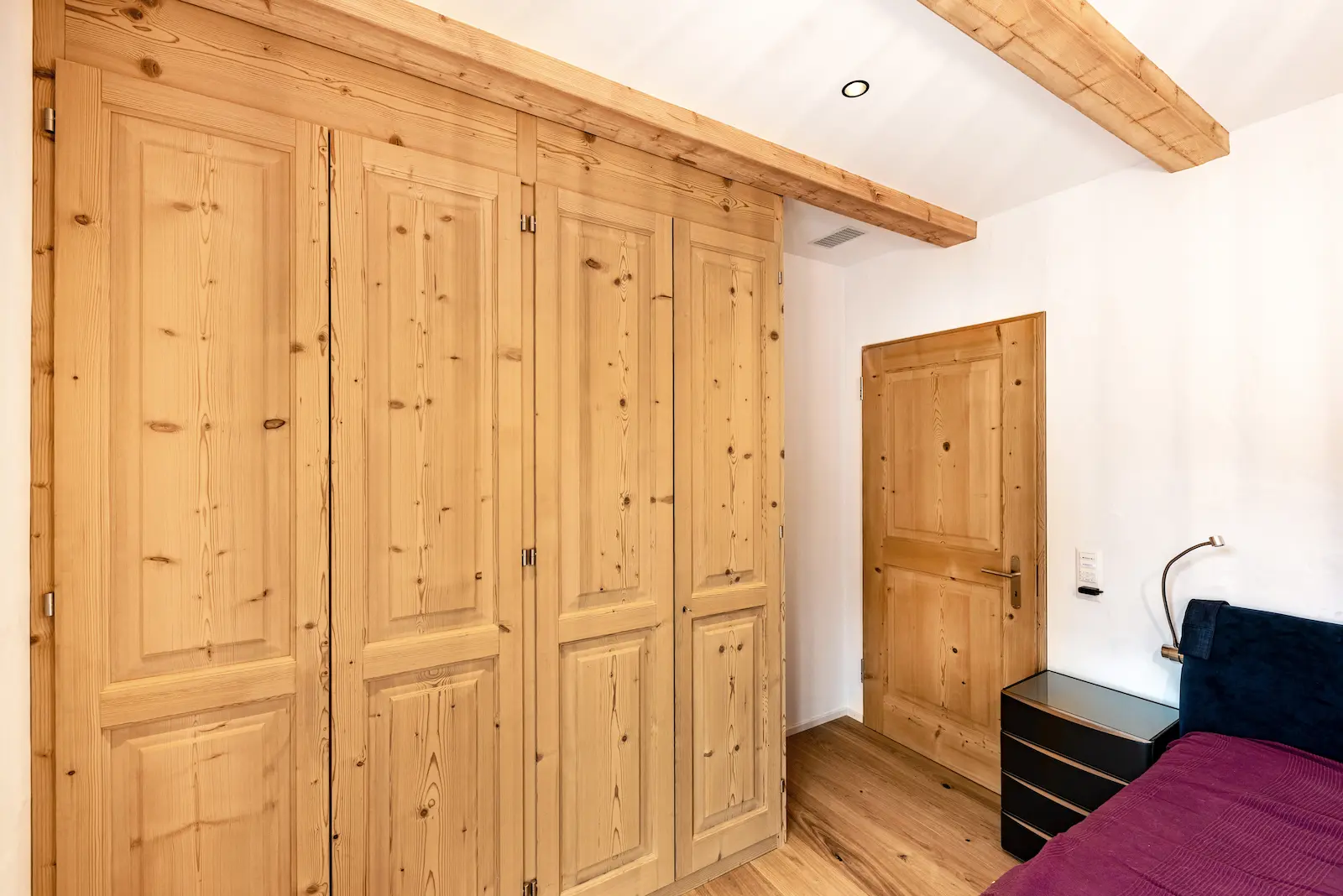 Massgefertigter Kleiderschrank aus gebürstetem Massivholz mit vier Türen und sichtbarer Maserung im Schlafzimmer.
