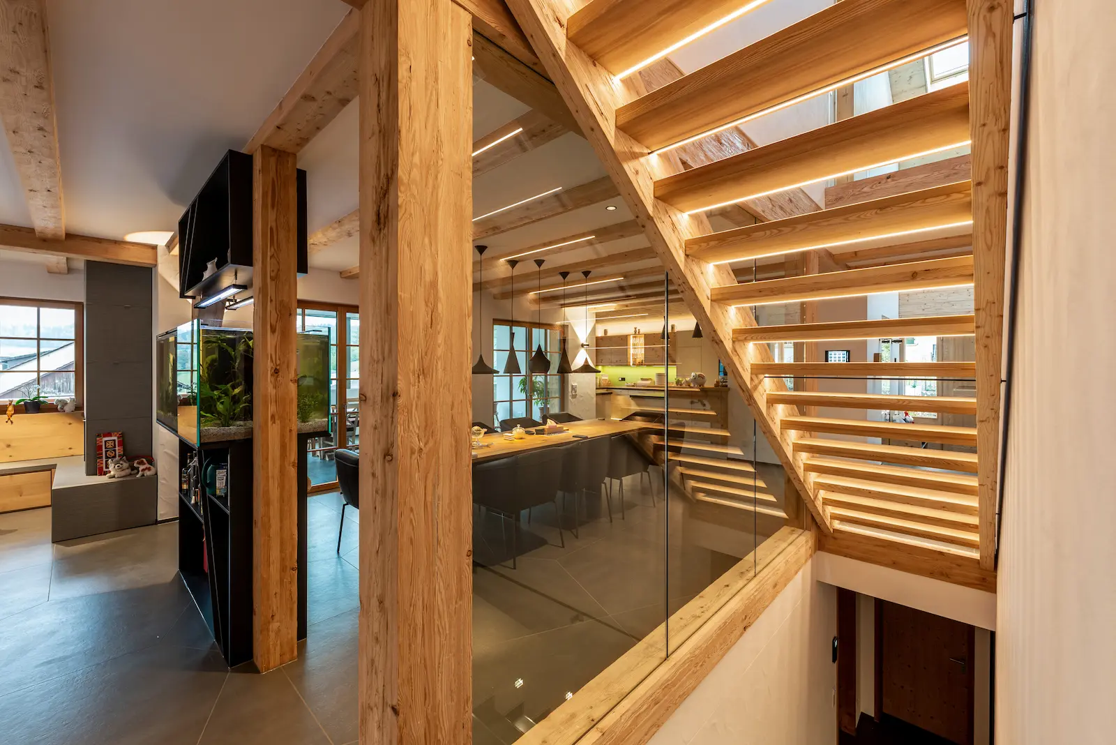Offenes Holztragwerk mit sichtbaren Lärchenpfosten, Glasgeländer und Treppe im Wohnbereich.