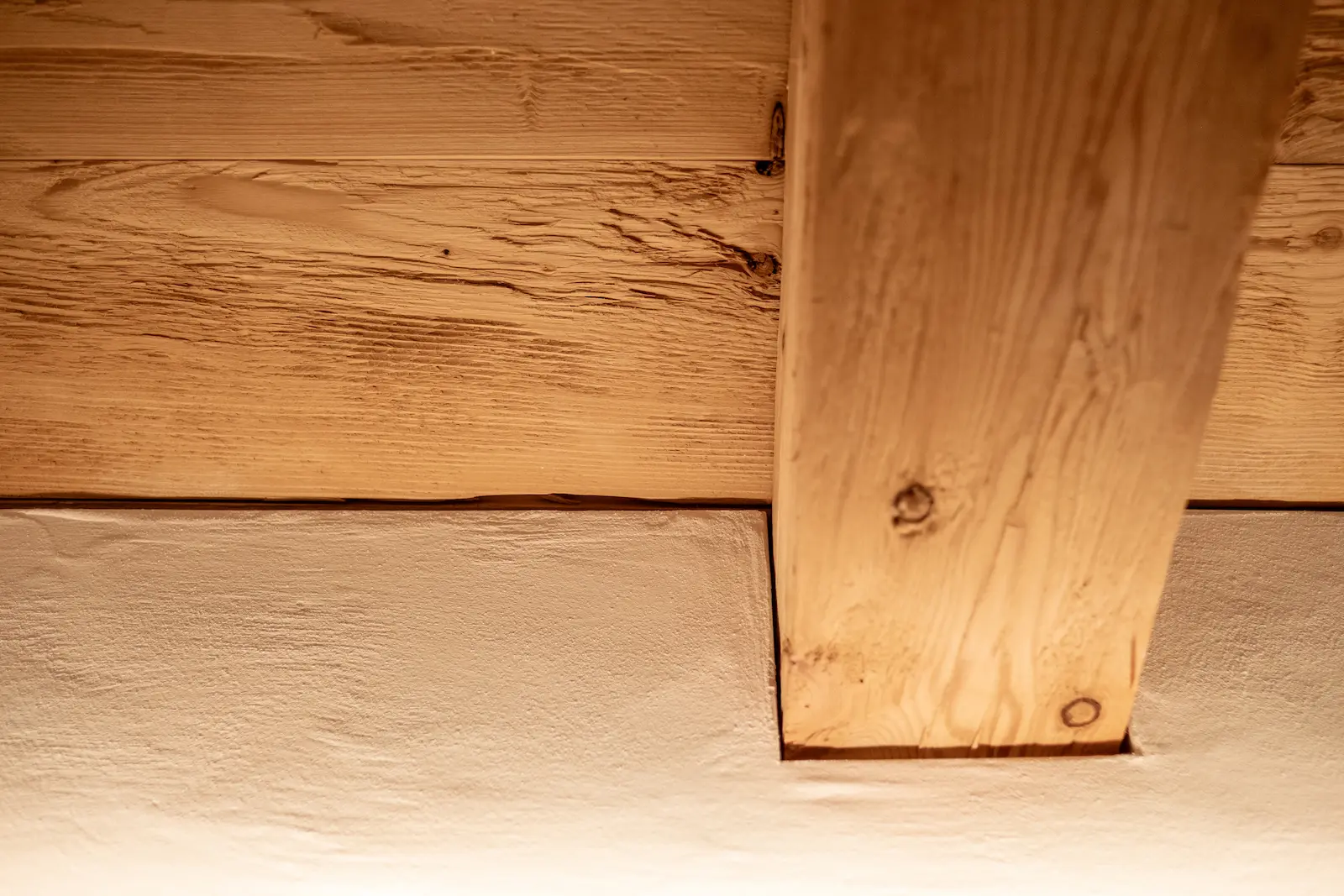 Detailfoto eines Übergangs zwischen Holzdecke und weisser Wandfläche.