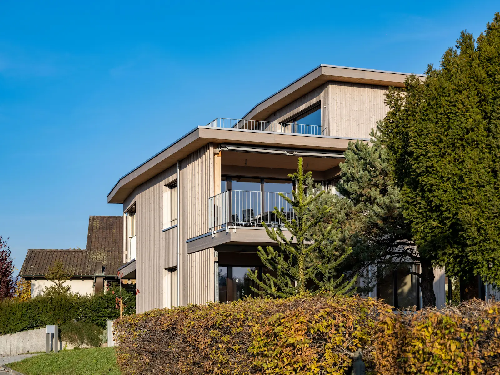 Gesamtansicht eines modernen Mehrfamilienhauses mit mehrstöckiger Holzfassade, Flachdach und vorgelagerten Balkonen, realisiert im Holzelementbau mit vorgefertigten Wand- und Fassadenelementen.