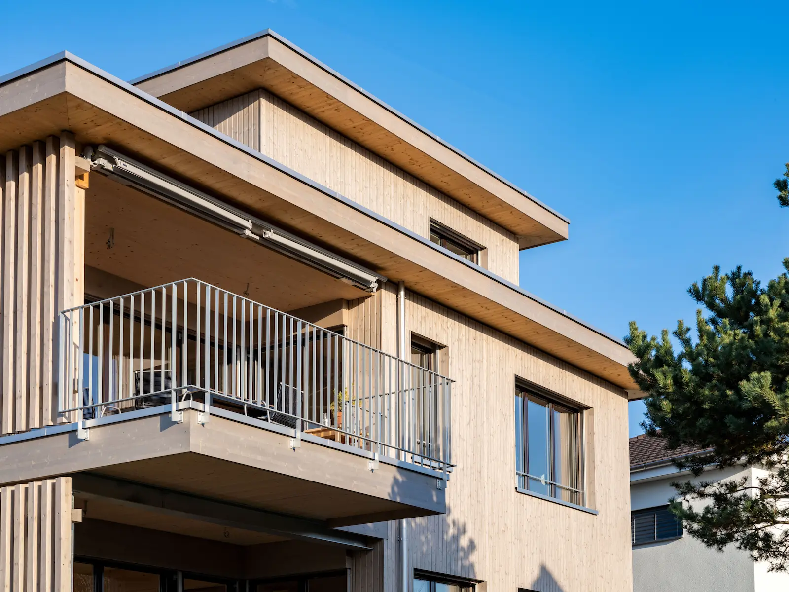 Balkon eines Mehrfamilienhauses in Holzsystembauweise, mit vertikaler Holzfassade aus nordischer Fichte und Metallgeländer, gefertigt in Elementbauweise.