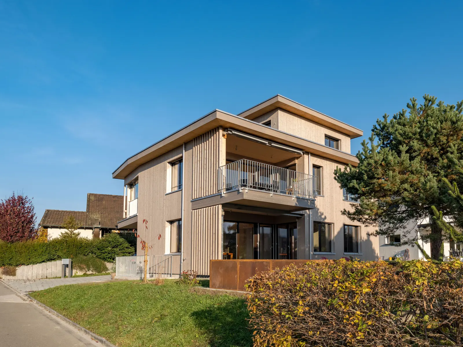 Gesamtansicht des Einfamilienhauses mit vertikaler Holzfassade, grossen Fensterflächen und vorgelagertem Balkonbereich.