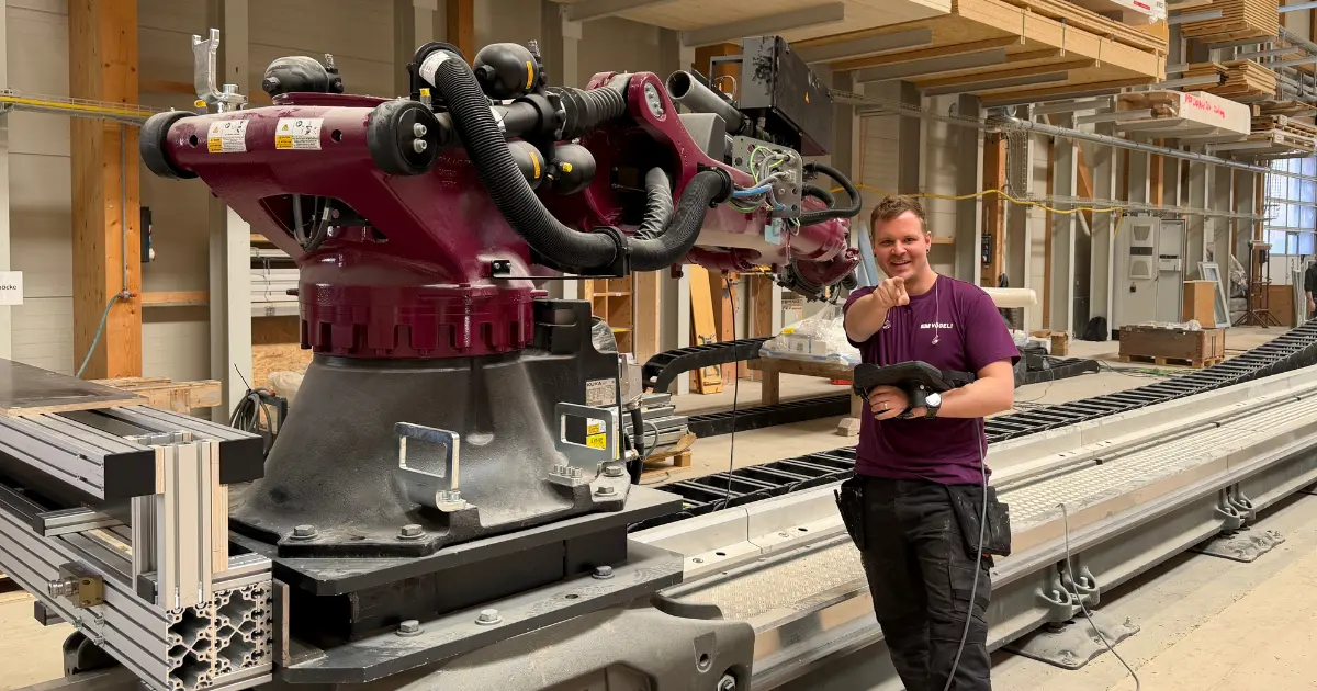 Ein Elementbauroboter mit einem Maschinisten in der Werkhalle von Vögeli Holzbau. Der Roboter sowie das T-Shirt des Maschinisten ist in der Farbe Aubergine.