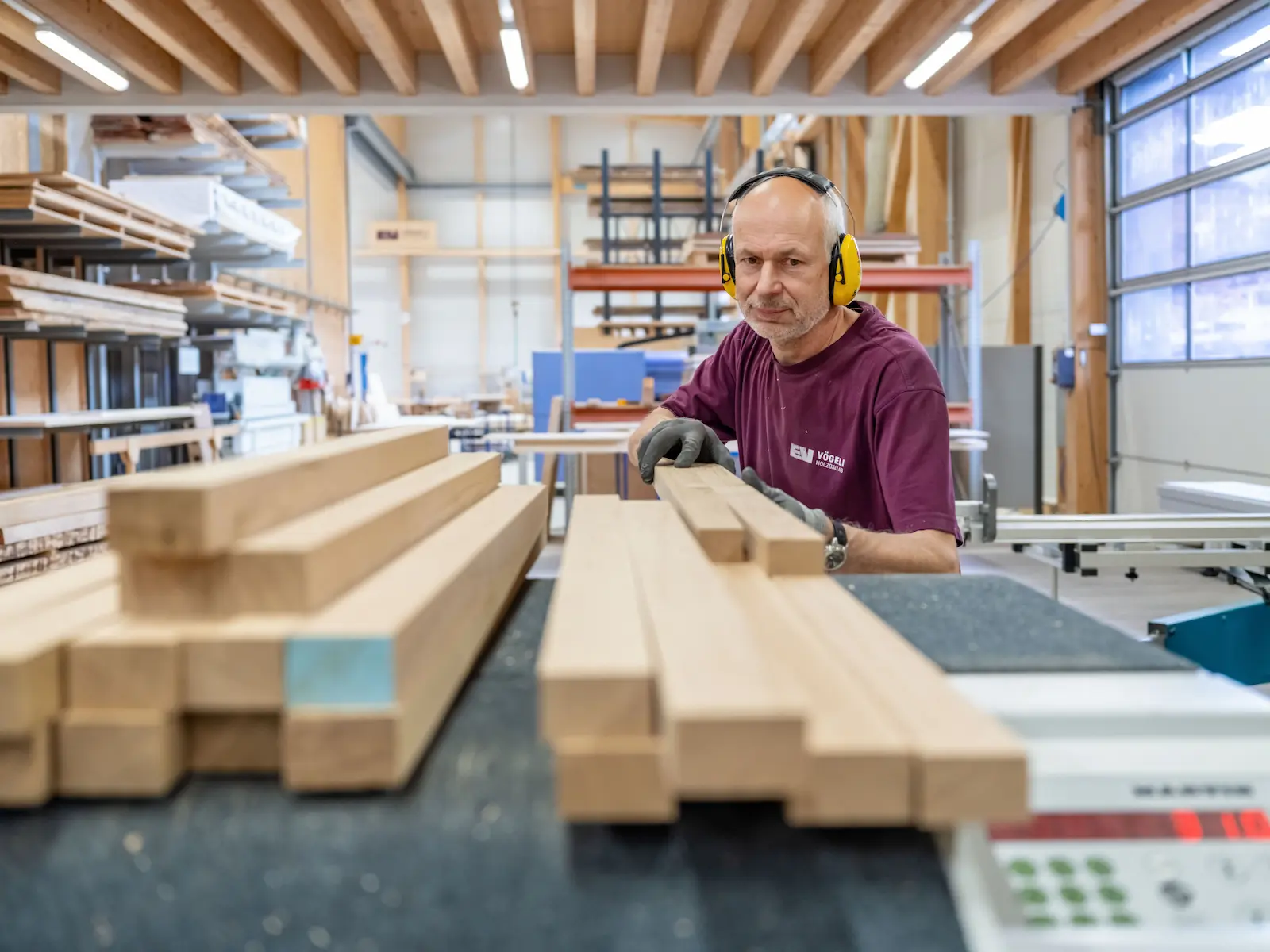 Zimmermann der Vögeli Holzbau AG bei der Arbeit in der topmodernen Produktionshalle — konzentriert, handwerklich präzise, mit Gehörschutz und Firmen-Shirt.
