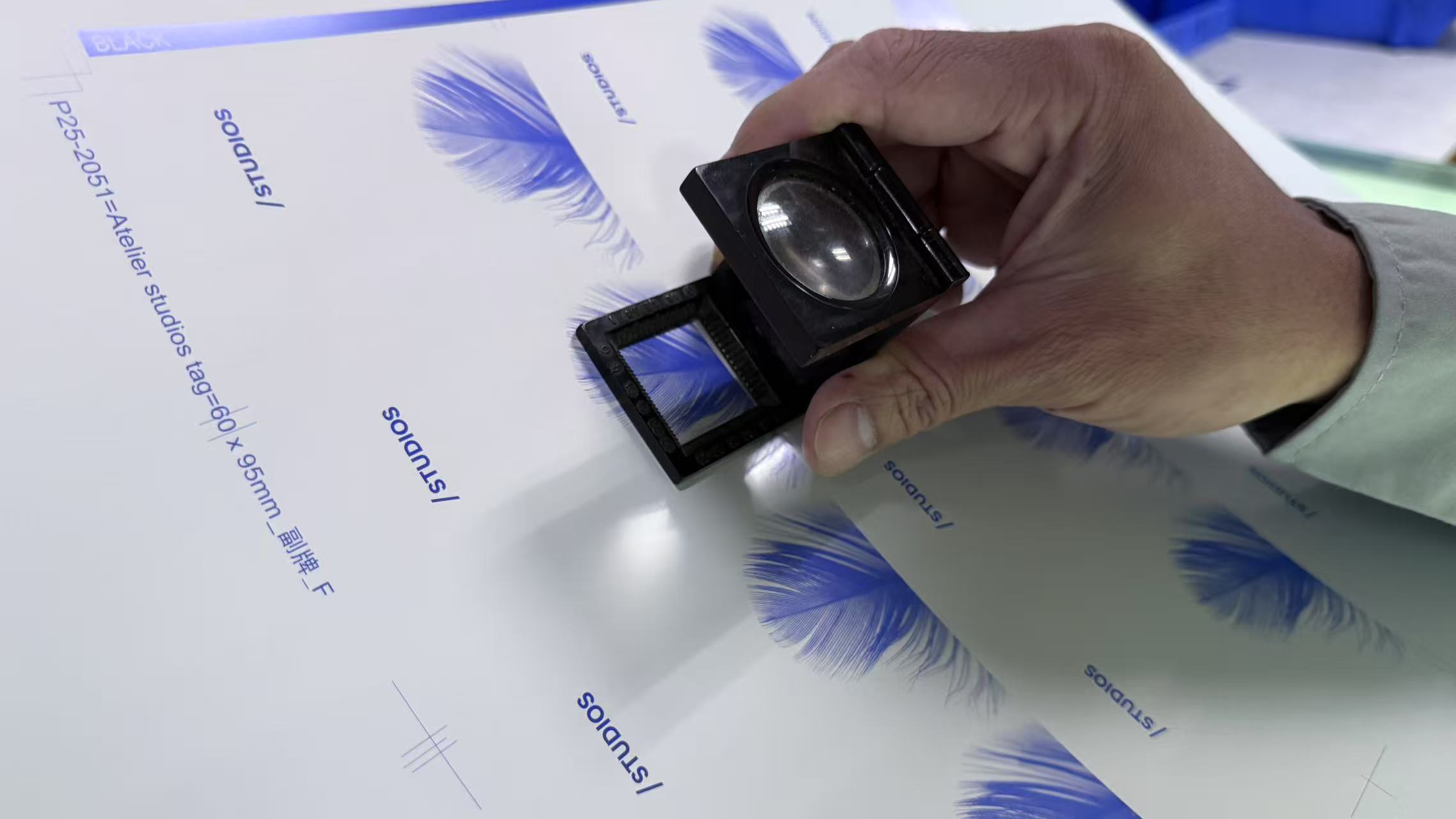 Hand holding a magnifying loupe over printed label artwork